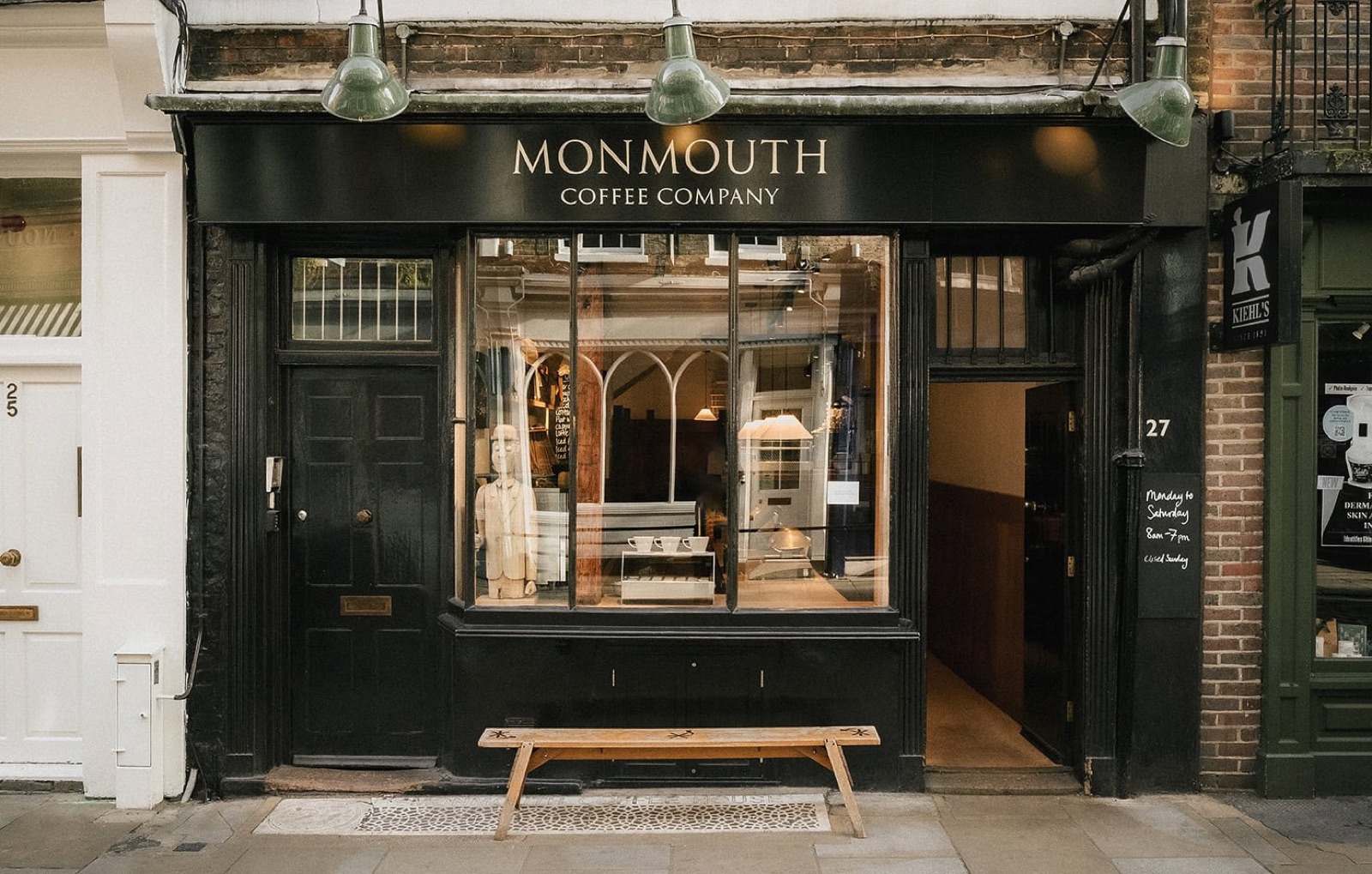 The black-fronted Monmouth Coffee Company storefront on Monmouth Street, hanging lamps above and a wooden bench outside