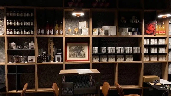 Wall to wall shelving of retail bottles, teas, and coffee tins around a framed print and small tasting table at Erikoffee
