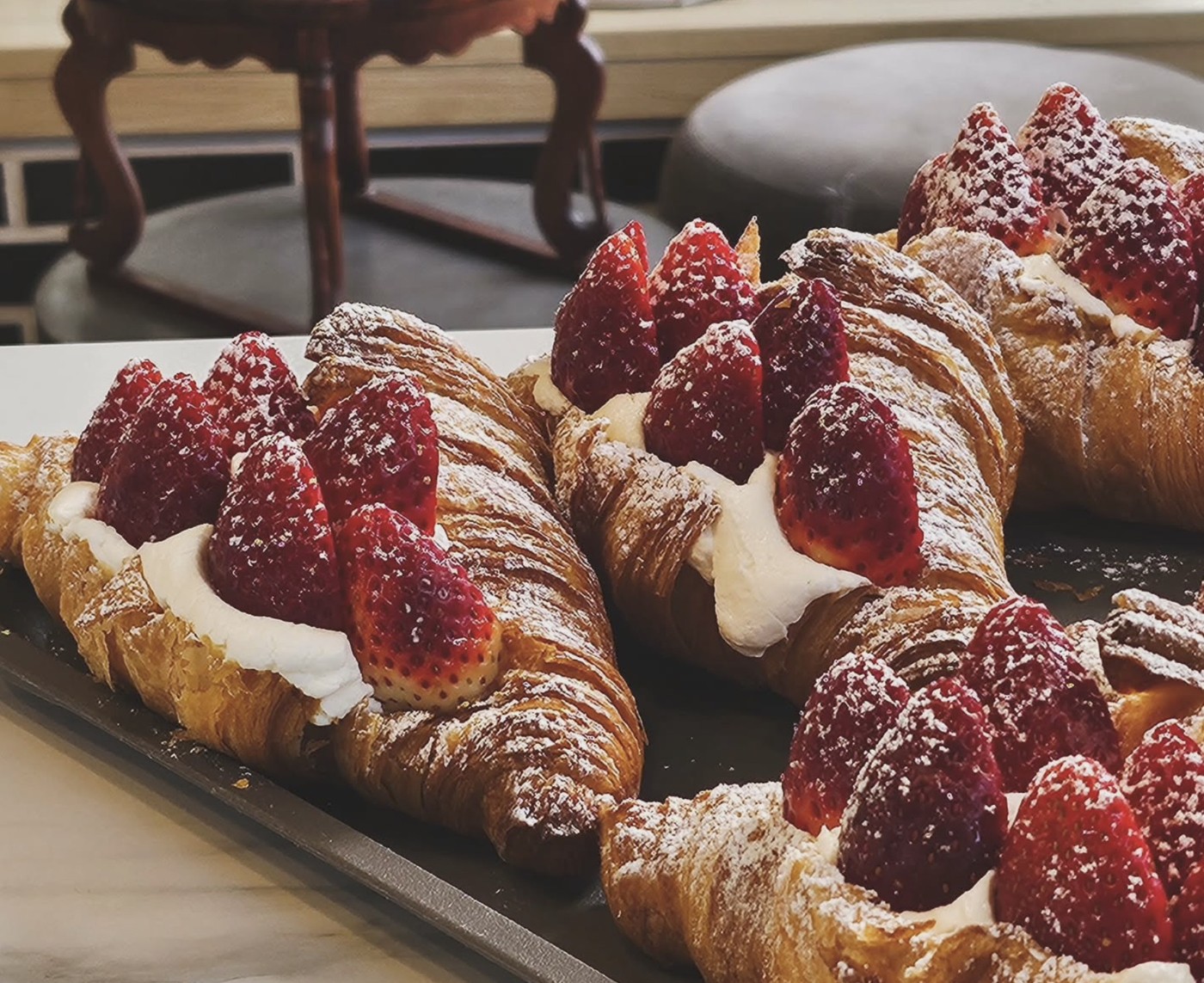 A row of cream and strawberry filled pastries dusted with powdered sugar on a tray at Kiwa Café