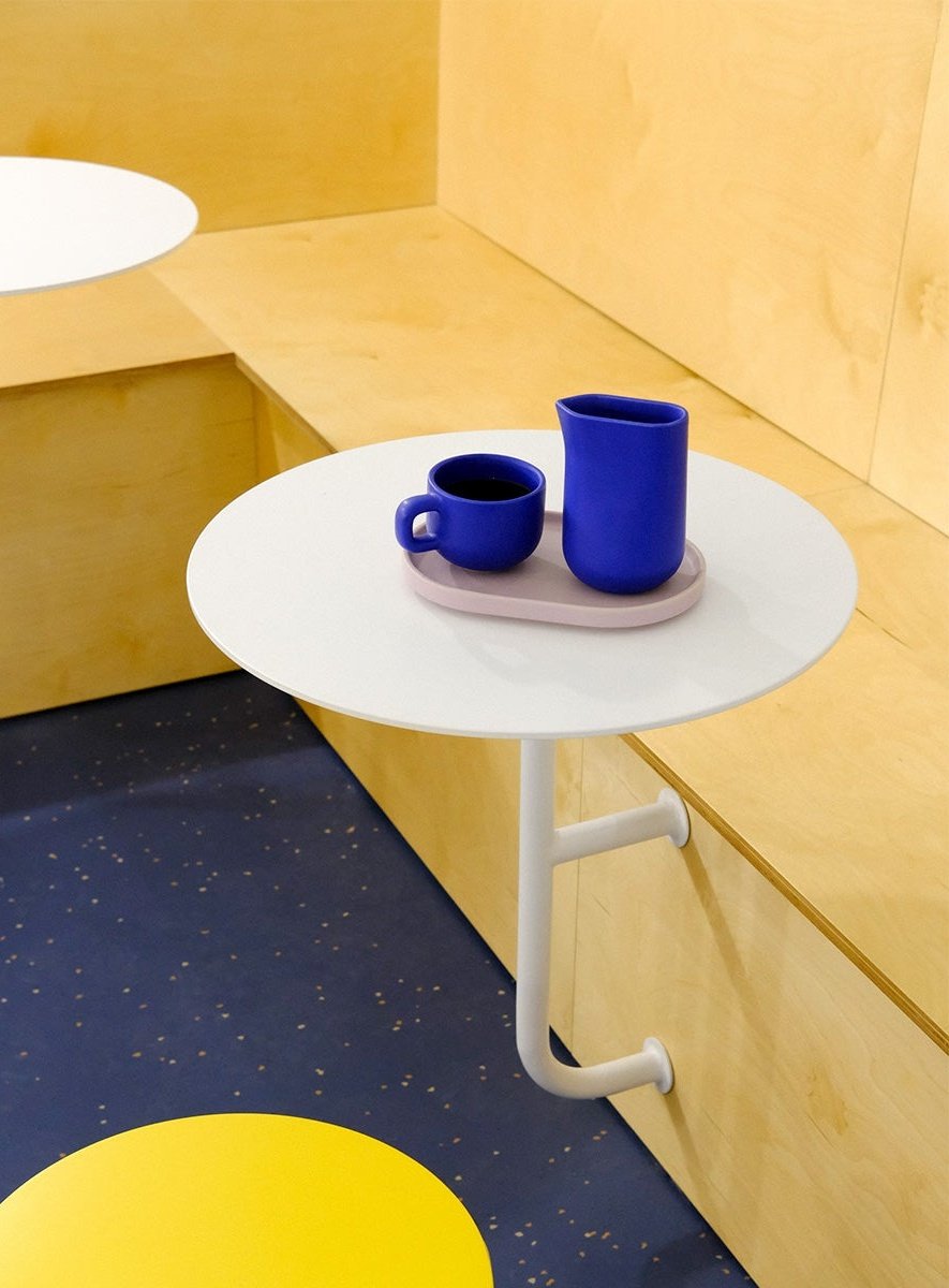 A side table at Hola Coffee with blue ceramic cups, plywood benches and a speckled terrazzo floor