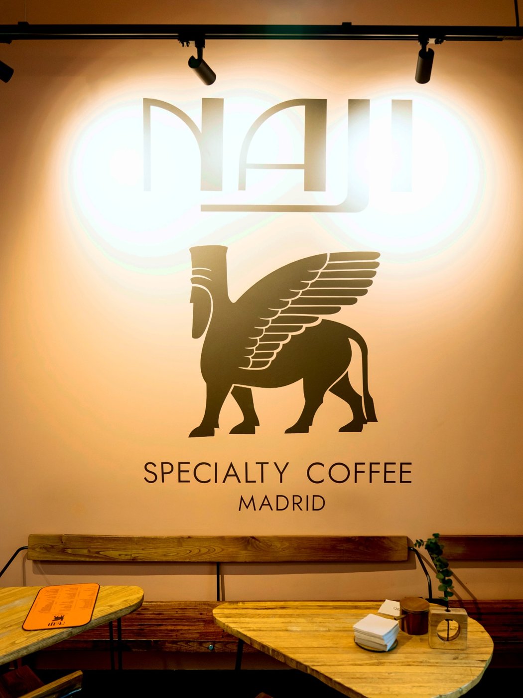 The winged-bull Naji Specialty Coffee logo on the wall above wooden bench seating
