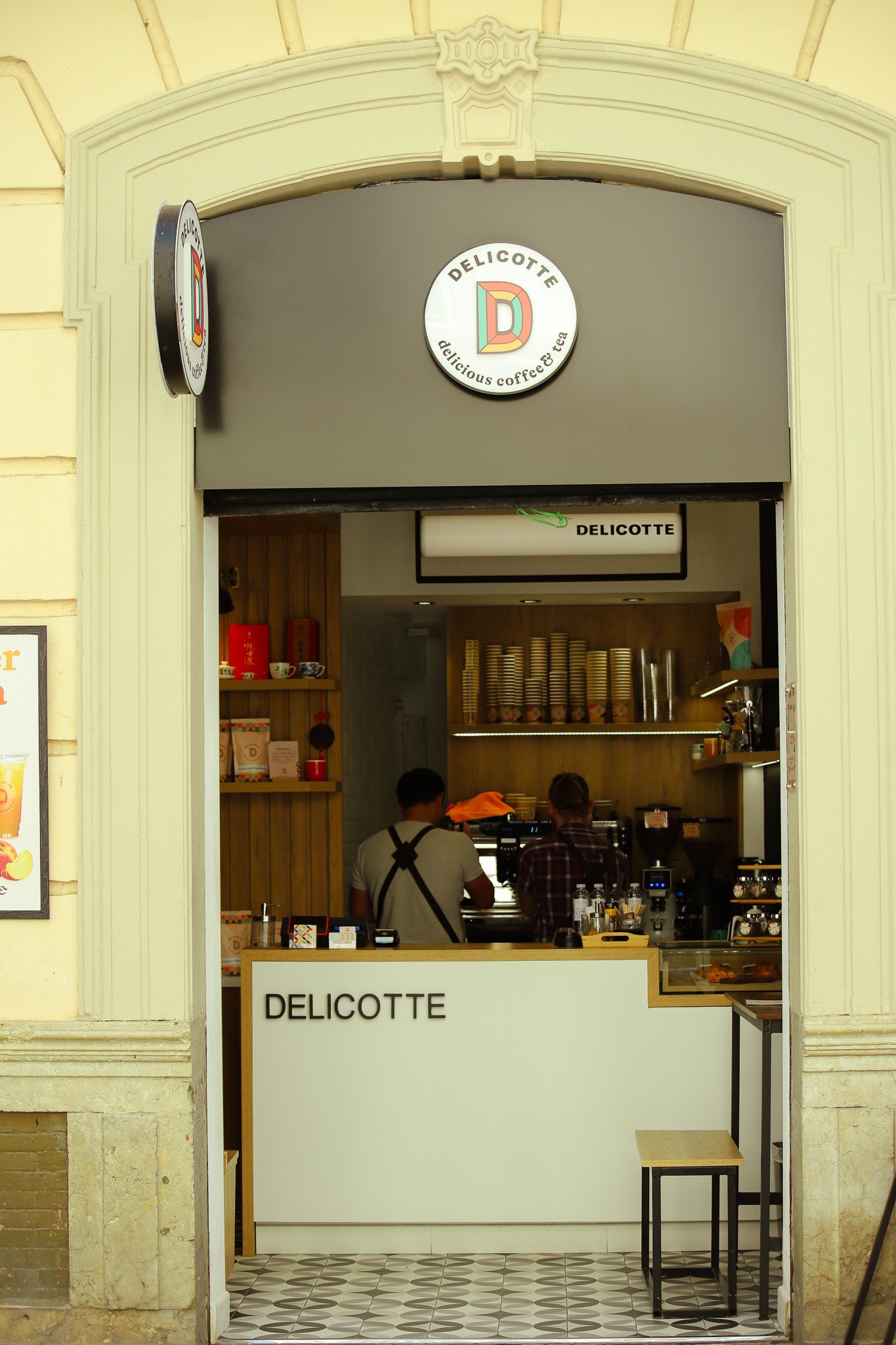 The Delicotte storefront sign reading delicious coffee and tea, with two baristas working the espresso counter inside