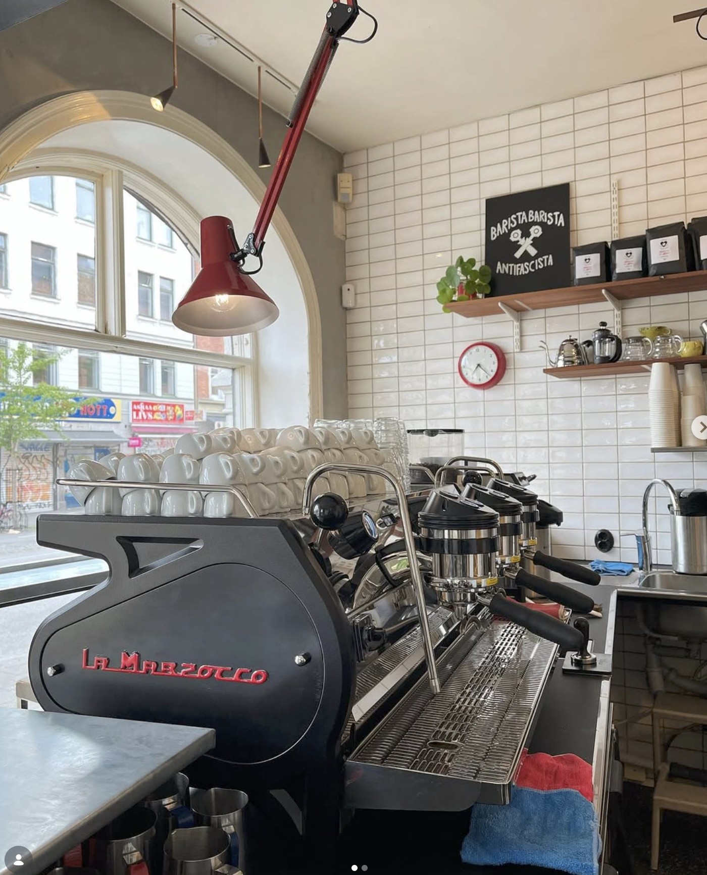 The La Marzocco espresso machine and stacked cups at Kaffebaren på Möllan, with a Barista Barista Antifascista sign on the tiled wall behind