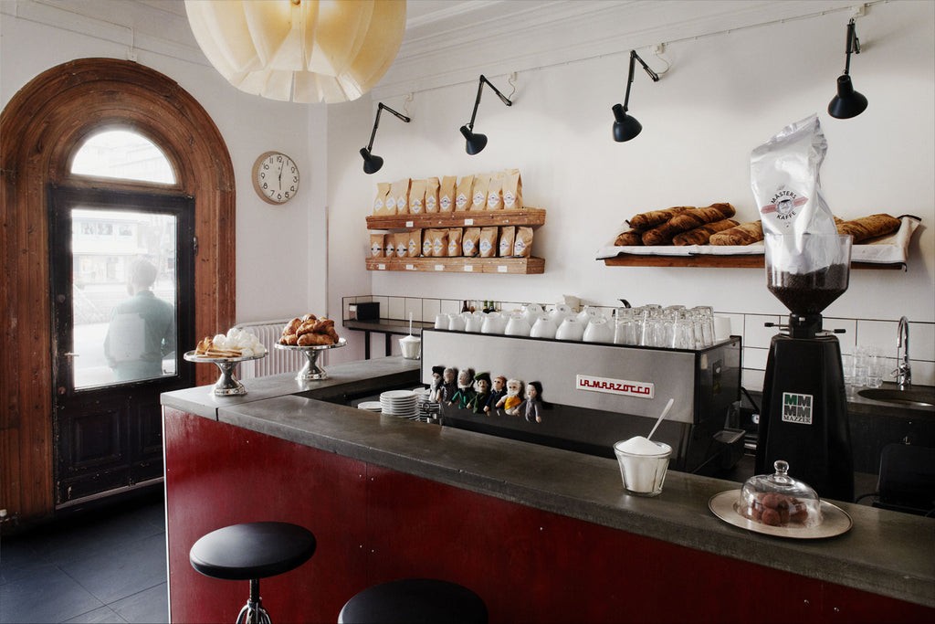 The Solde counter with a La Marzocco machine, retail bean bags labeled Mäster's Kaffe, and an arched wooden door