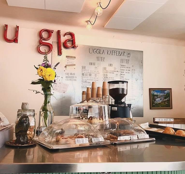 The counter at Uggla Kaffebar with its neon owl sign, chalkboard menu, and pastry display