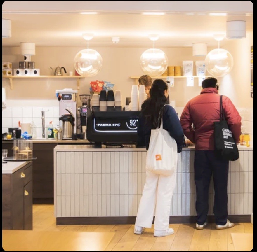 Customers ordering at the counter under globe pendant lights, with the branded 92 espresso machine in the foreground