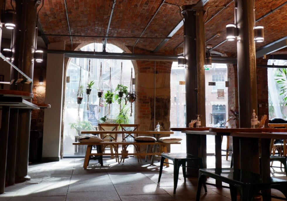 The brick vaulted interior of Ancoats Coffee Co. with hanging plants over the entrance arch and wooden bench seating