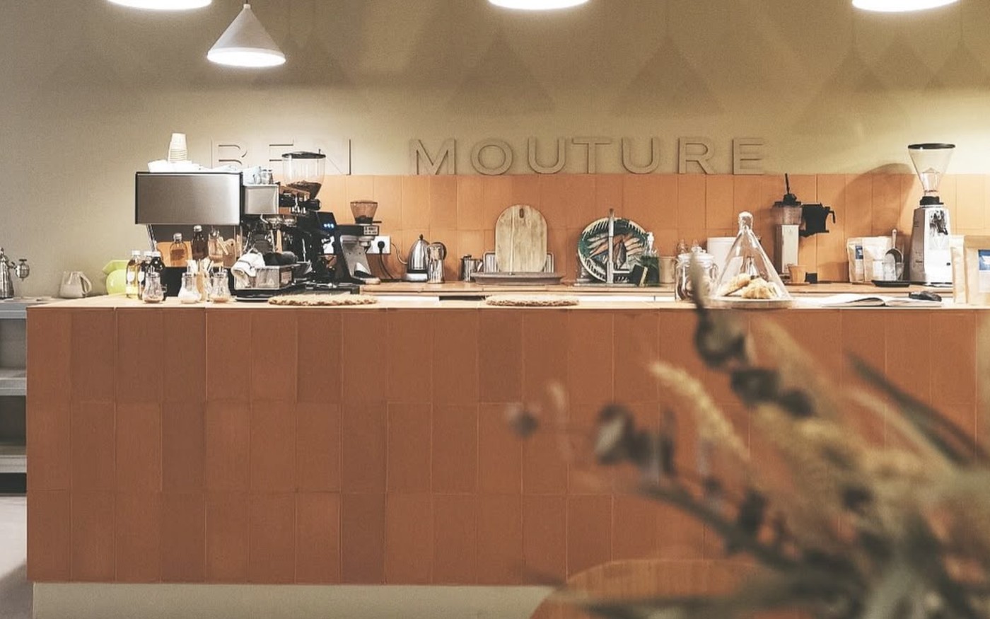 The counter at Ben Mouture with the name carved into the wall above the espresso bar and grinders, a dried flower arrangement in the foreground