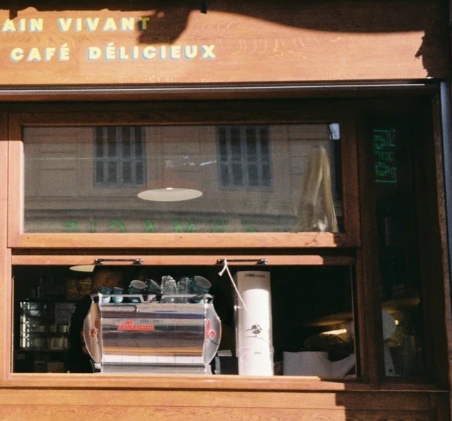The Pétrin Couchette storefront window, with the espresso machine visible at the counter beneath the Pain Vivant et Café Délicieux sign