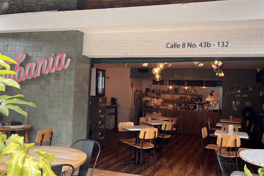 The Urbania Café storefront on Calle 8 in El Poblado, with the green tiled wall, the street address above the opening and the wooden bar and tables inside