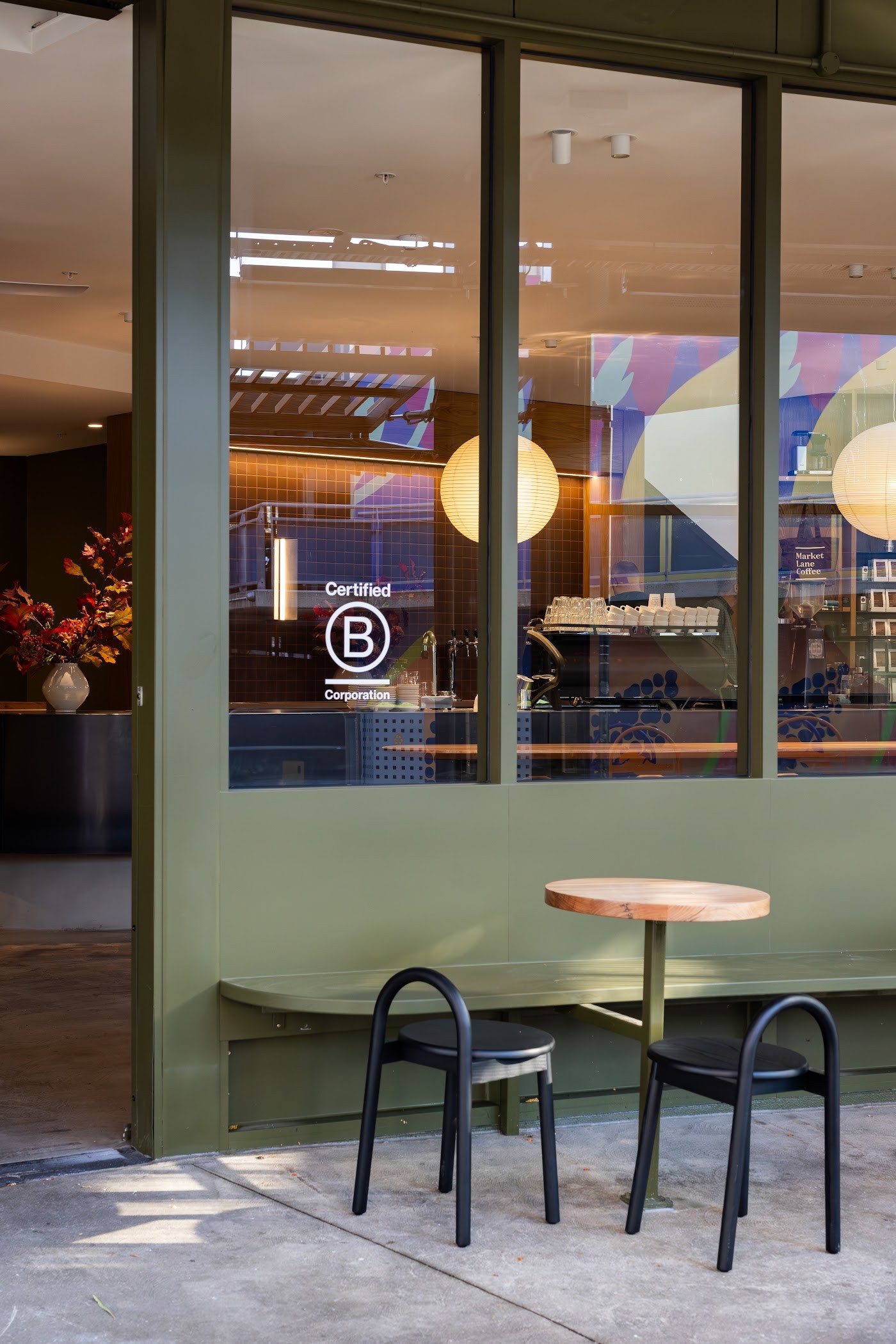 The green framed Market Lane Coffee storefront window at Prahran Market, with a Certified B Corporation decal and outdoor cafe seating