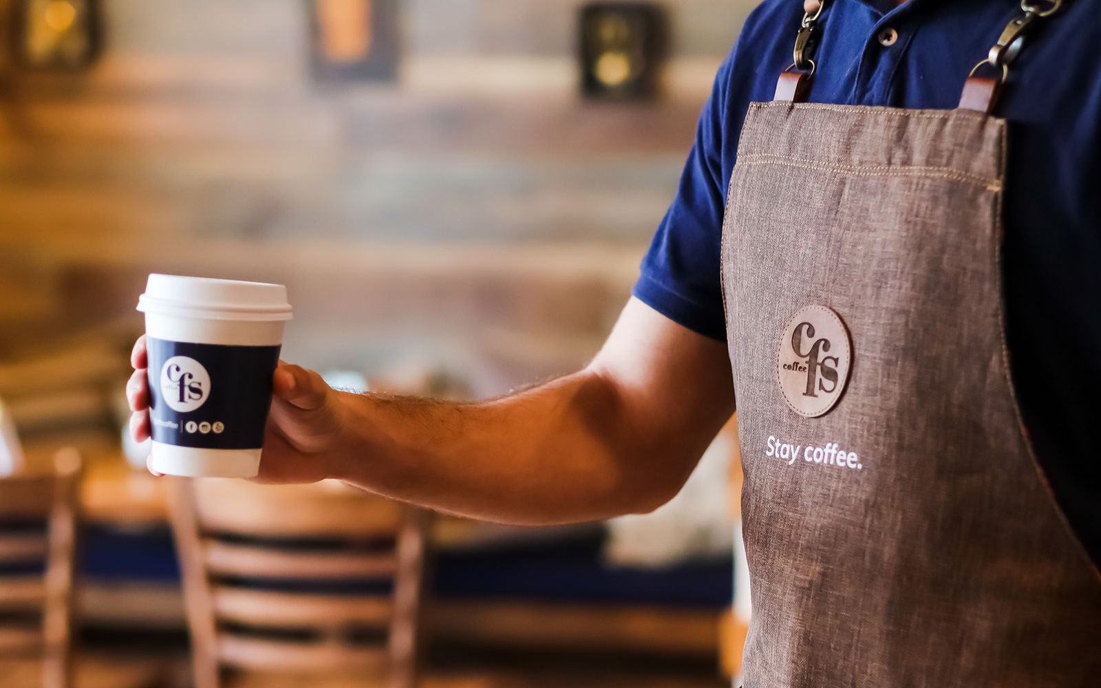 A branded CFS to go cup held out by a barista wearing the CFS apron