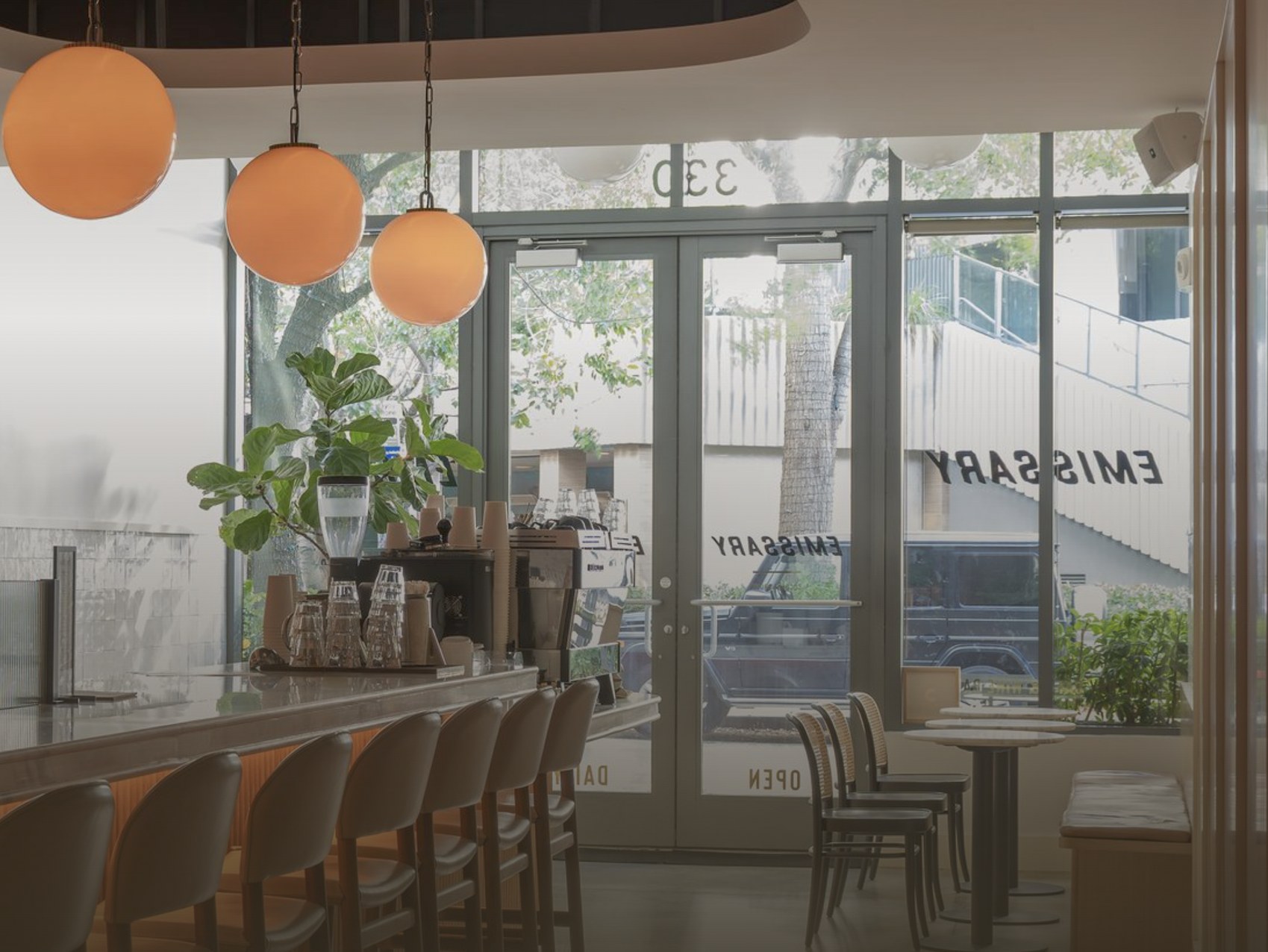 The counter and dining room at Emissary, with round orange pendant lights and a view through the storefront glass