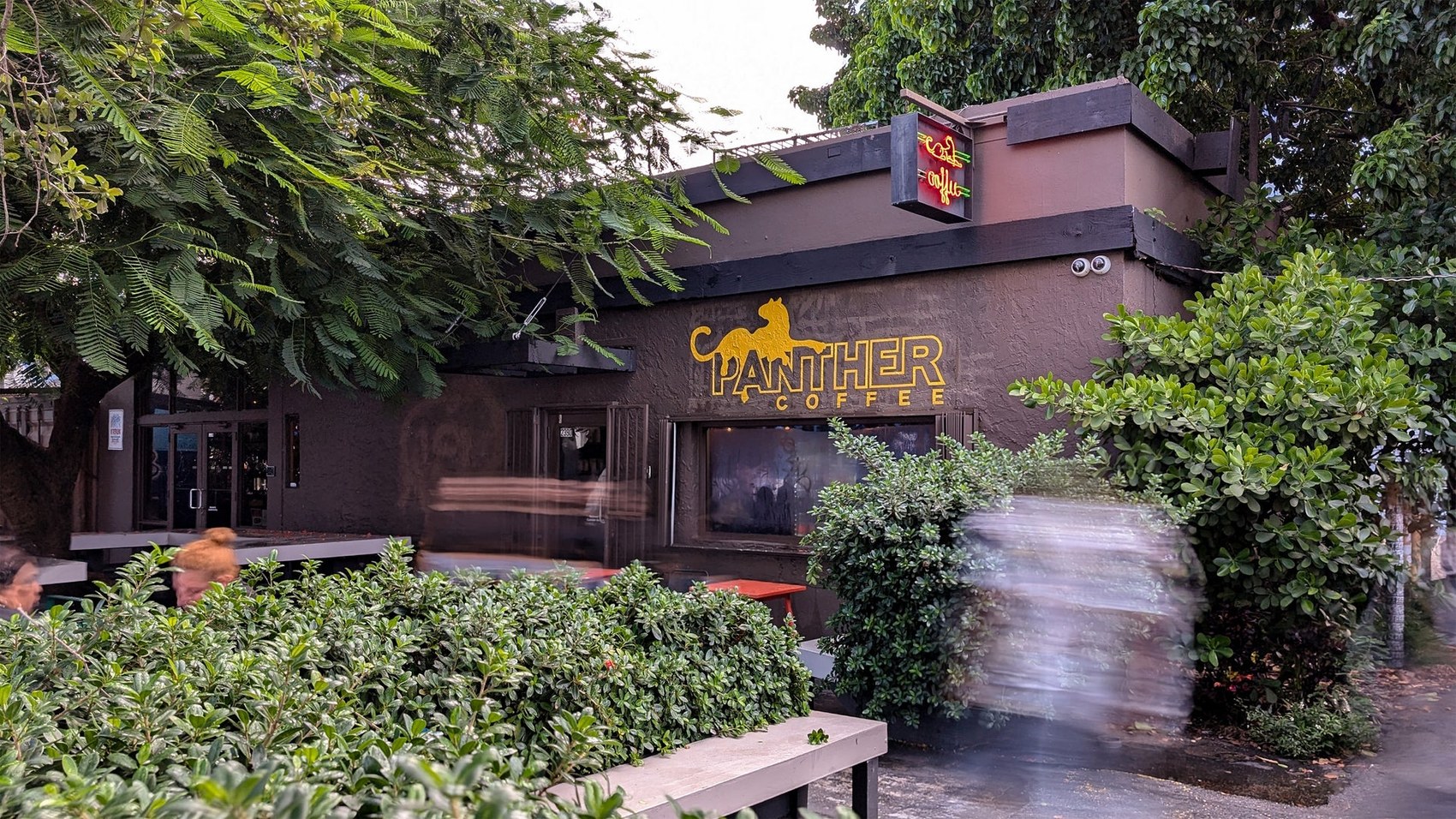 The Wynwood storefront at Panther Coffee with the neon sign and hedge lined patio