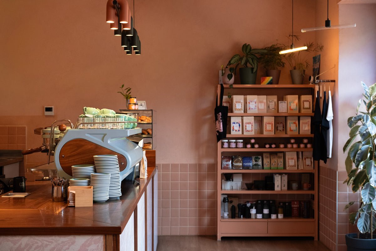 The pink-toned interior of Nowhere, espresso machine on the counter and a shelf of retail coffee bags