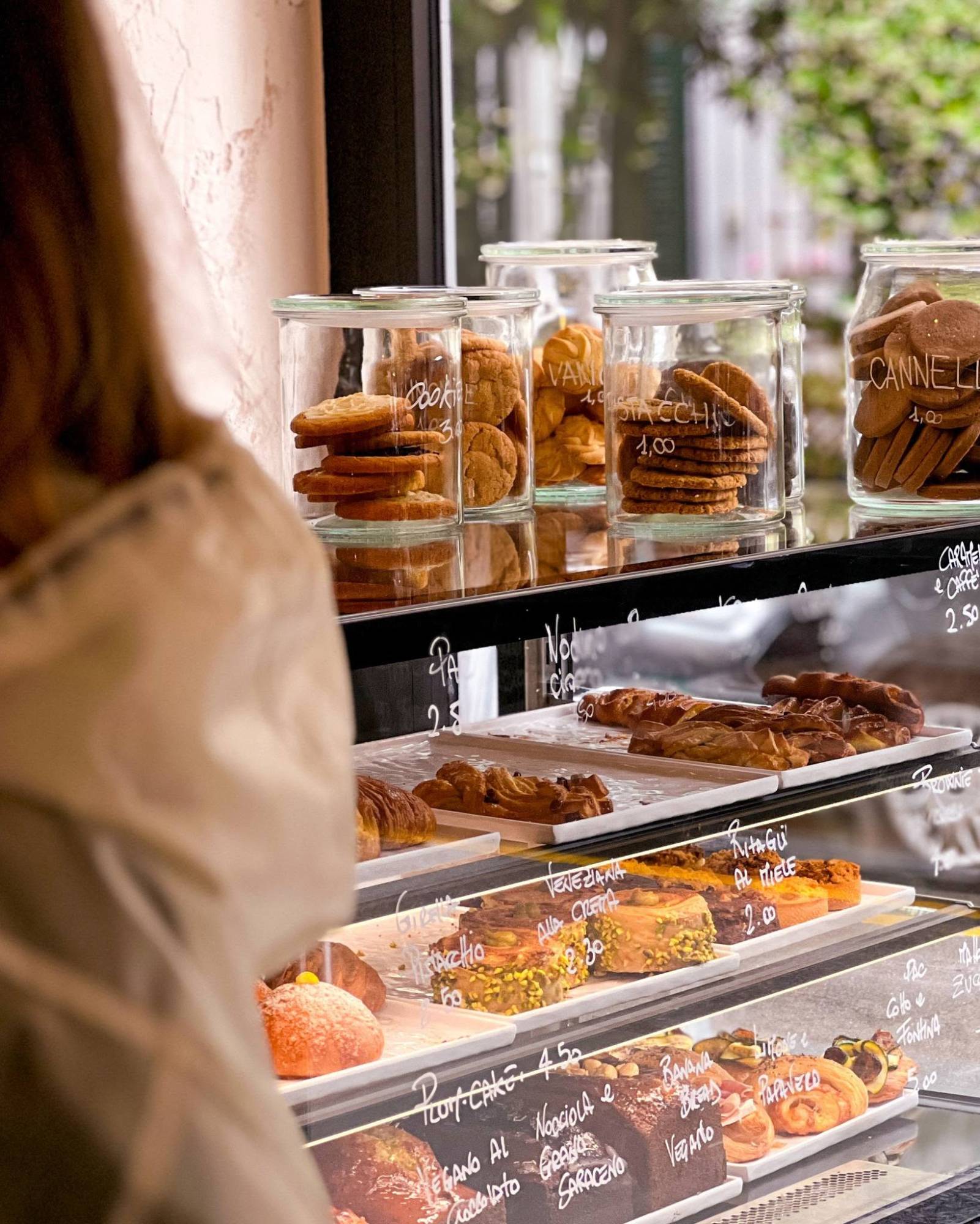The pastry counter at Sisu, glass jars of cookies labelled in white pen above a lit case of veneziane, croissants and cakes with handwritten Italian prices