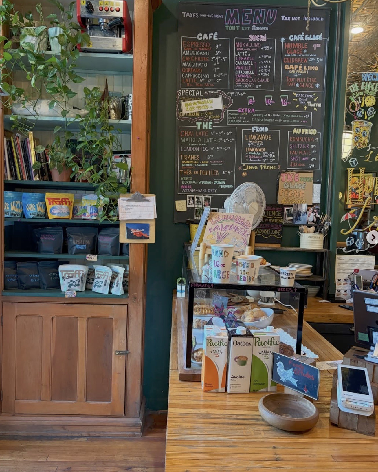 The counter at Cafe Humble Lion with a hand chalked menu board, shelves of house roasted bags, plants, and a pastry case up front