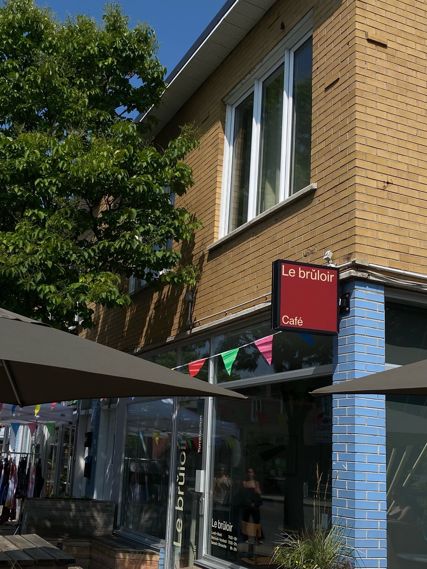 The Le brûloir Café sign mounted on the brick corner of the building, with festive bunting strung across the storefront windows below