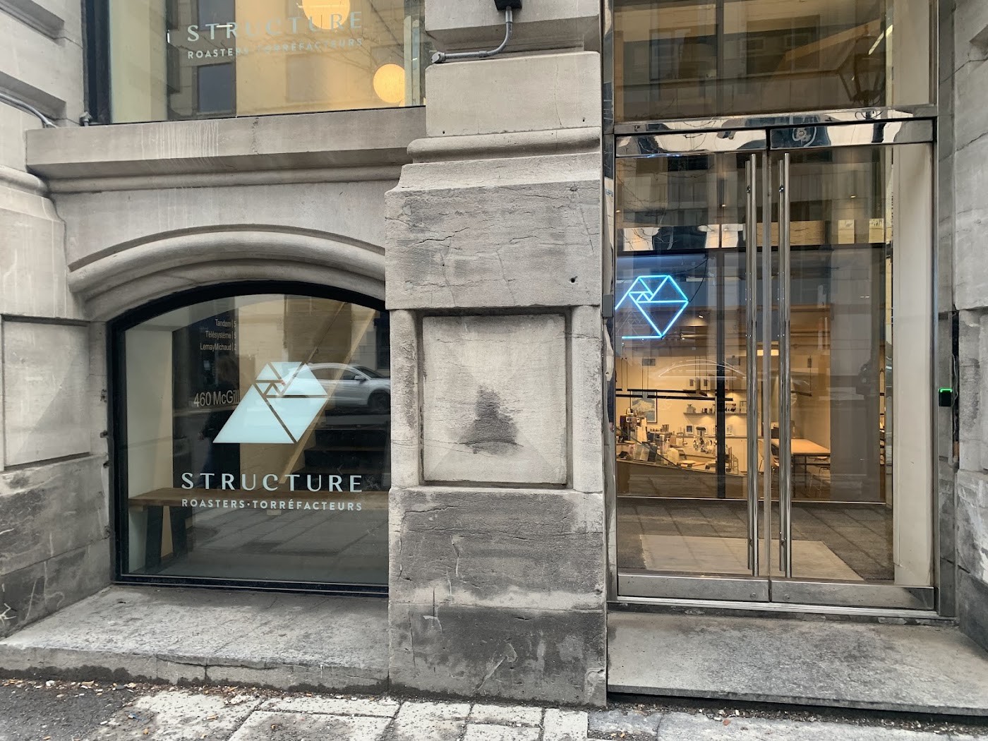 The stone facade at 460 Rue McGill with the Structure Roasters logo etched on the window and a glowing blue geometric sign visible through the glass entrance