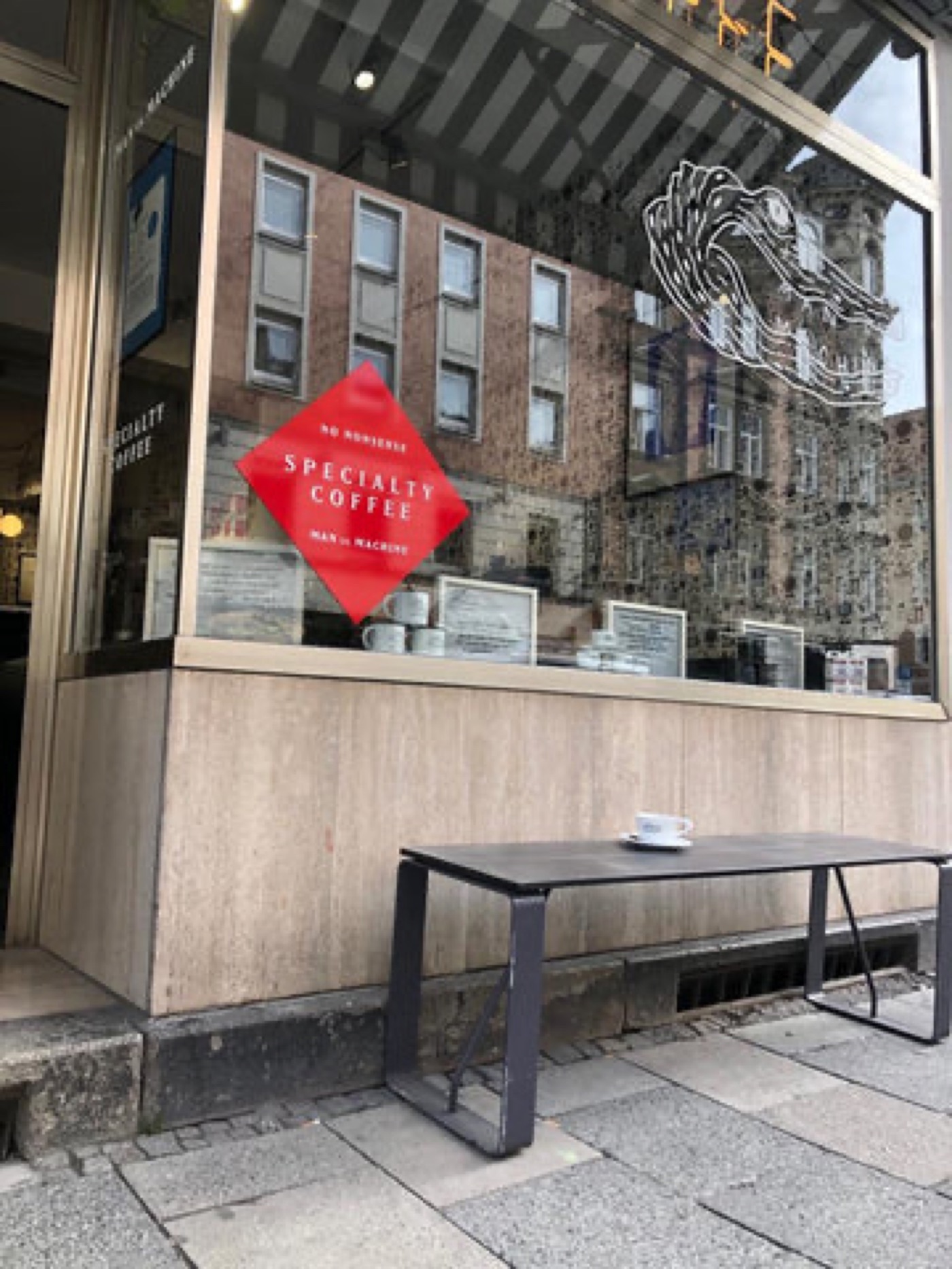 The storefront window of Man Versus Machine, a red diamond specialty coffee decal beside the shop's crocodile logo