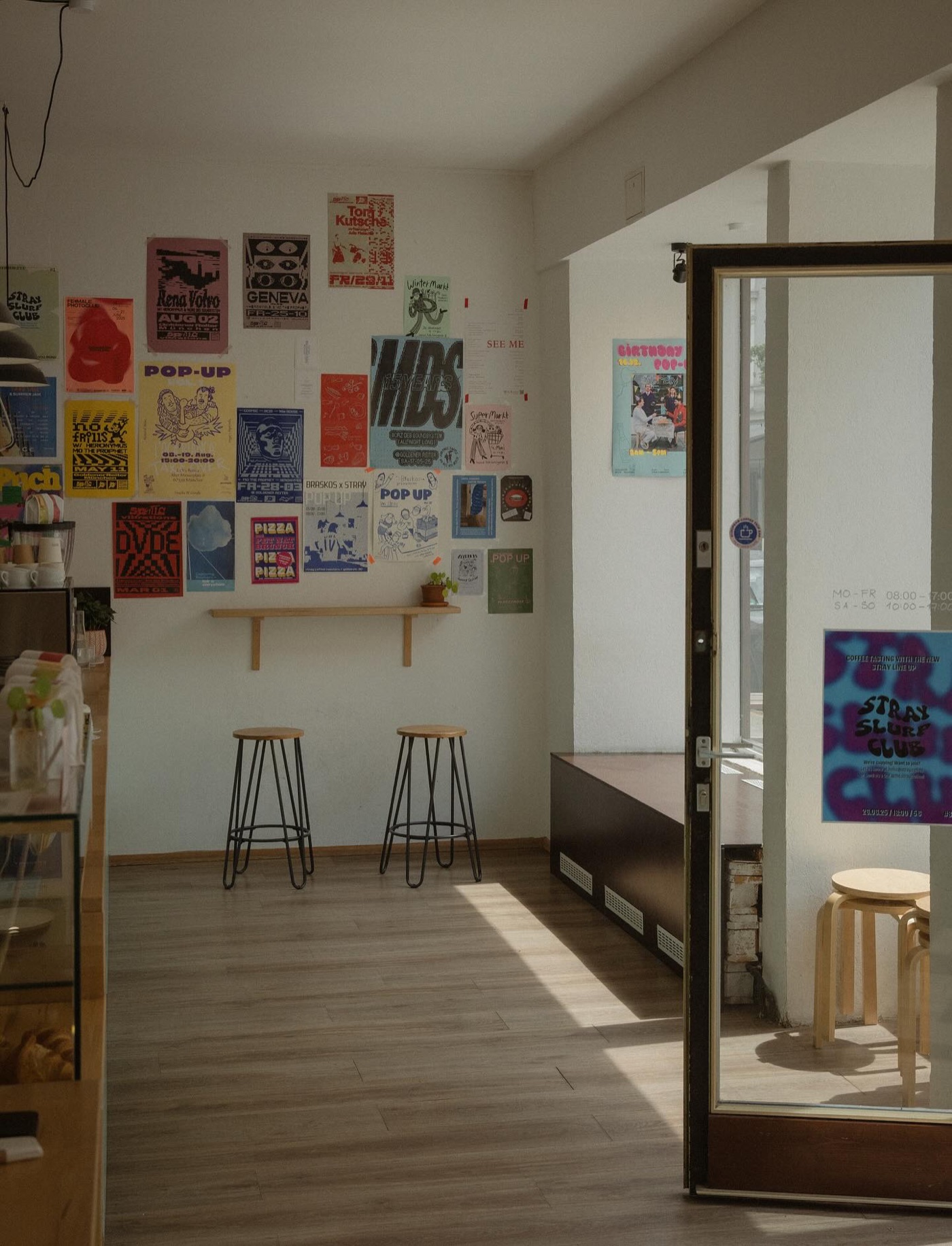 A wall covered in colorful gig posters and event flyers above two bar stools at Stray Coffee Roasters