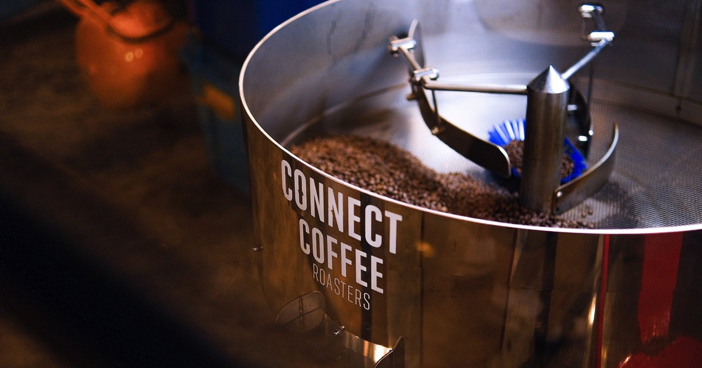 Fresh roasted coffee beans in a branded Connect Coffee Roasters cooling tray with a mixing arm