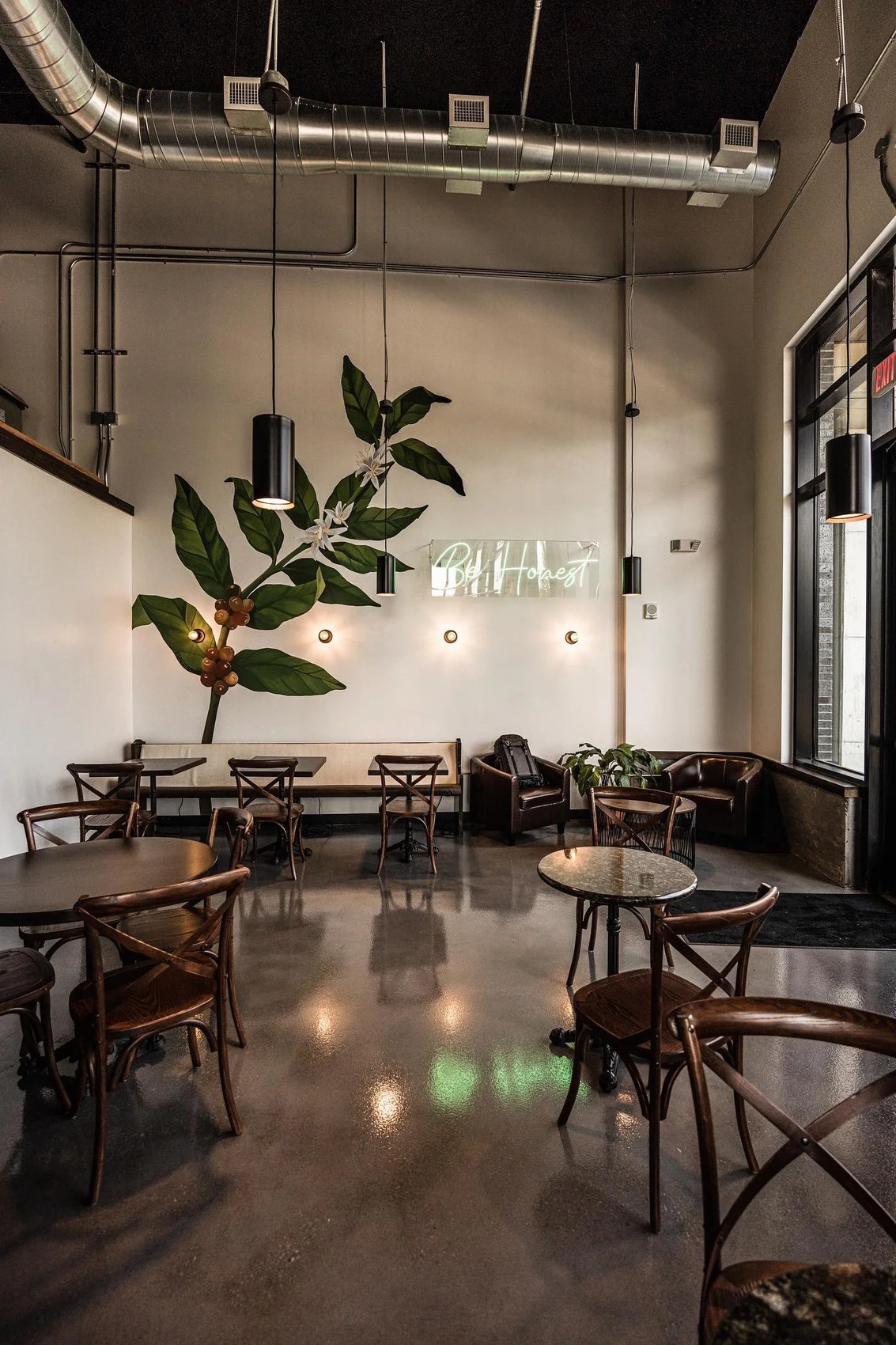 The seating area beneath a coffee plant mural and Be Honest neon sign at Honest Coffee Roasters