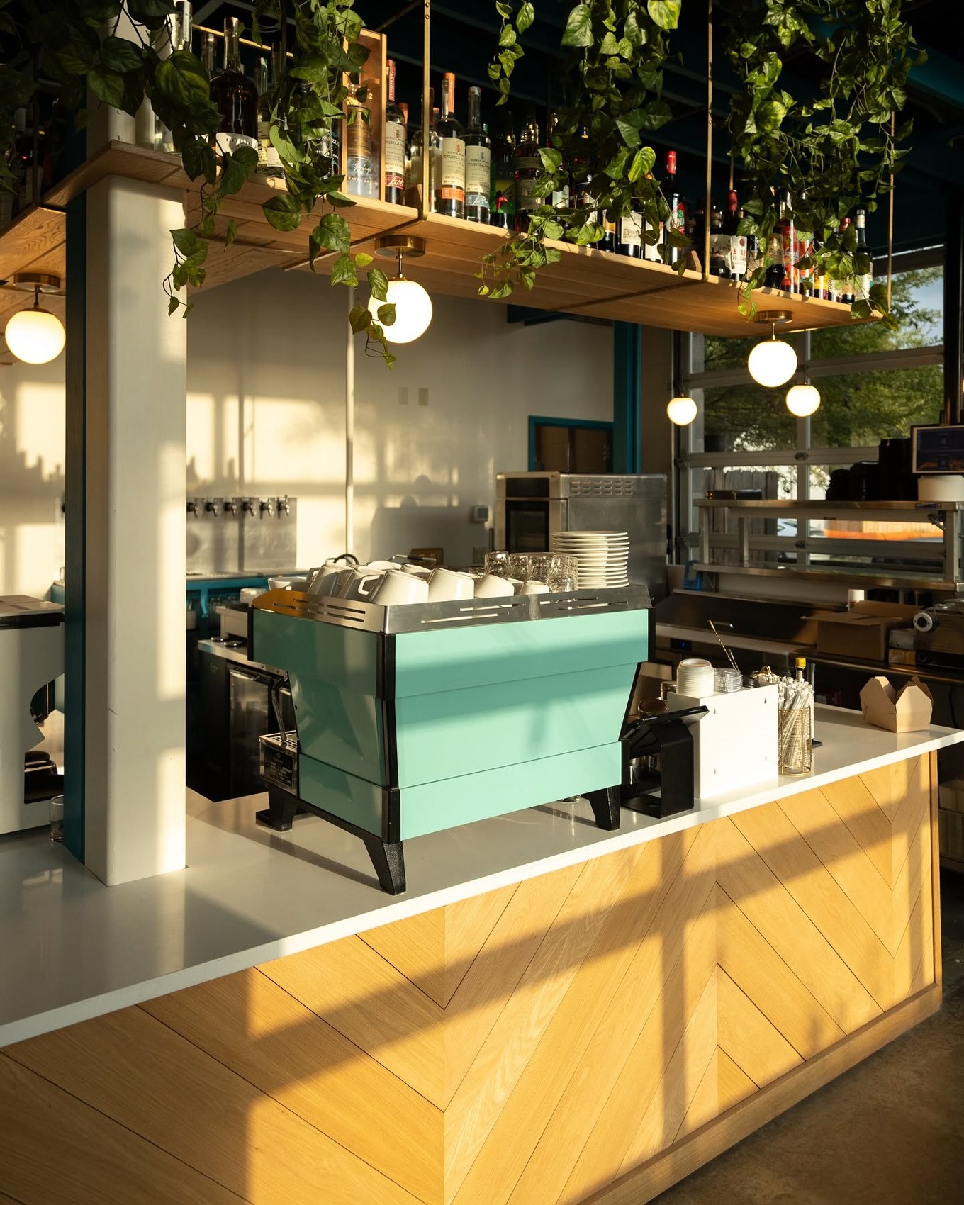 The teal espresso machine beneath the hanging liquor shelf at Stay Golden