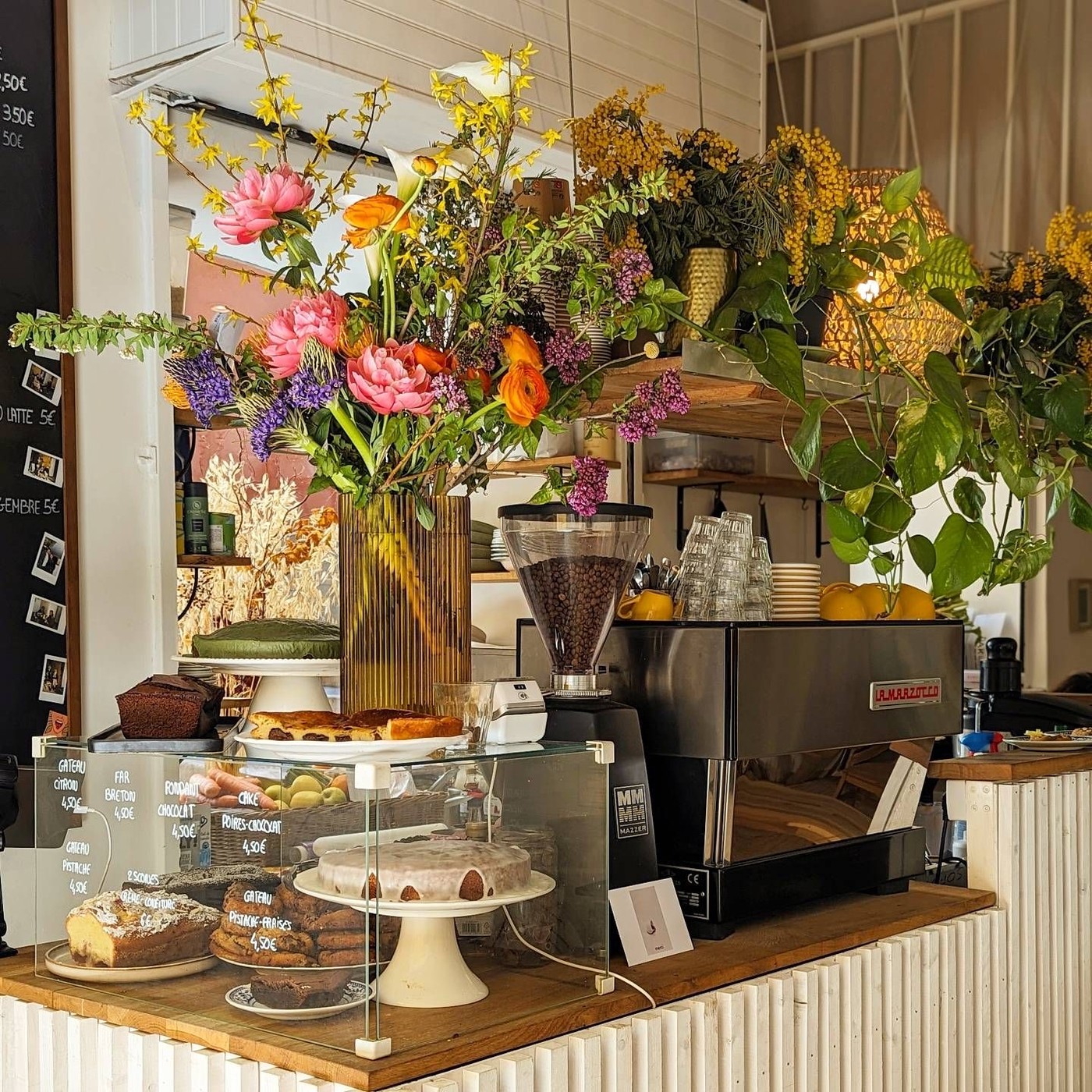 A wild flower arrangement above the espresso machine at Brume Coffee, with a glass case of cakes and pastries on the counter below