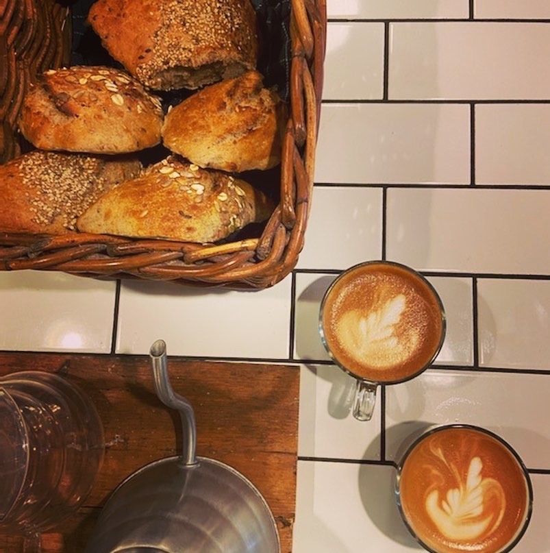 A bread basket and two cups of latte art coffee on white subway tile at Analog