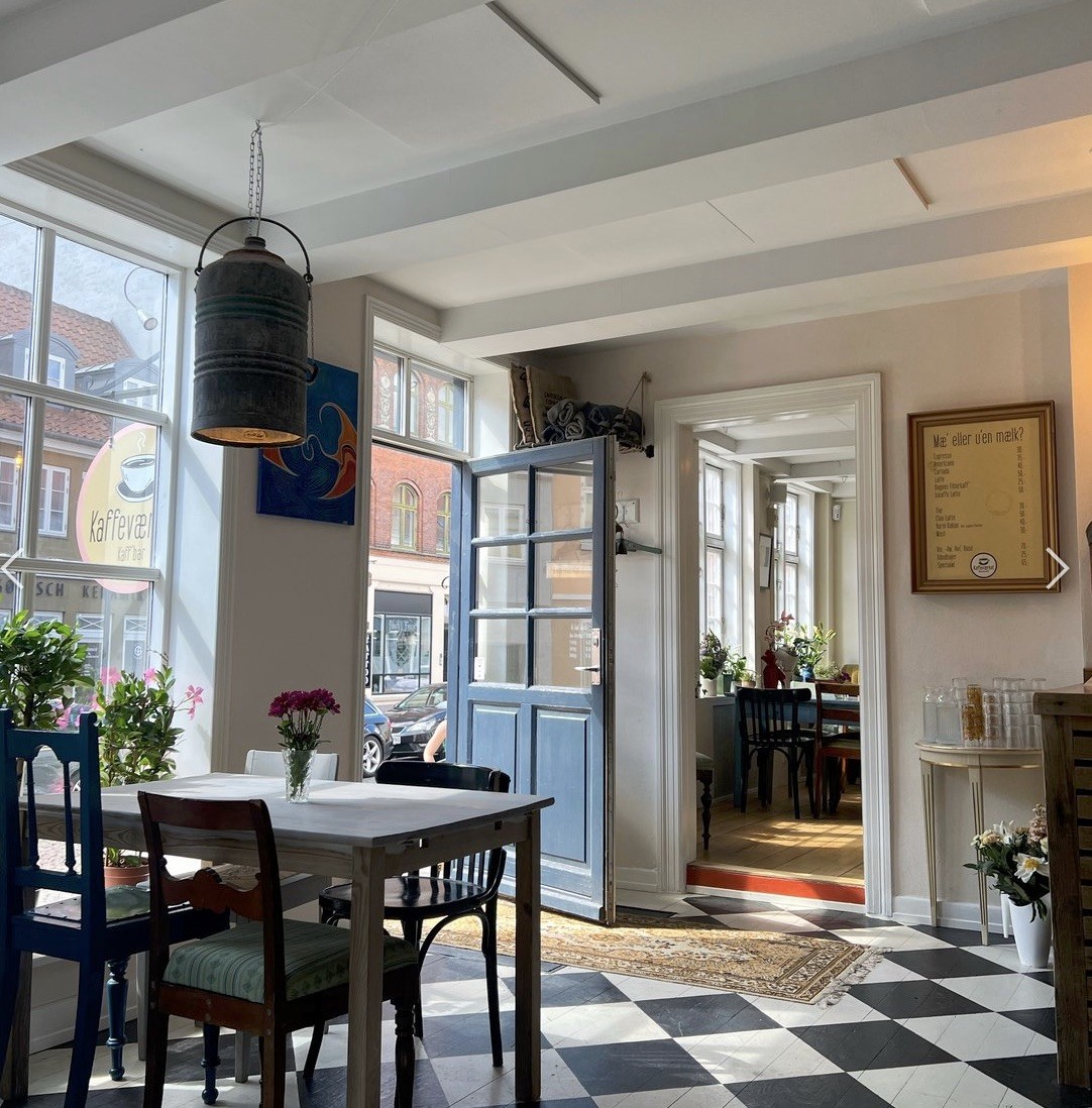 The exposed timber framed dining room at Kaffeværket with a checkerboard floor, blue front door, and a Kaffeværket sign in the window