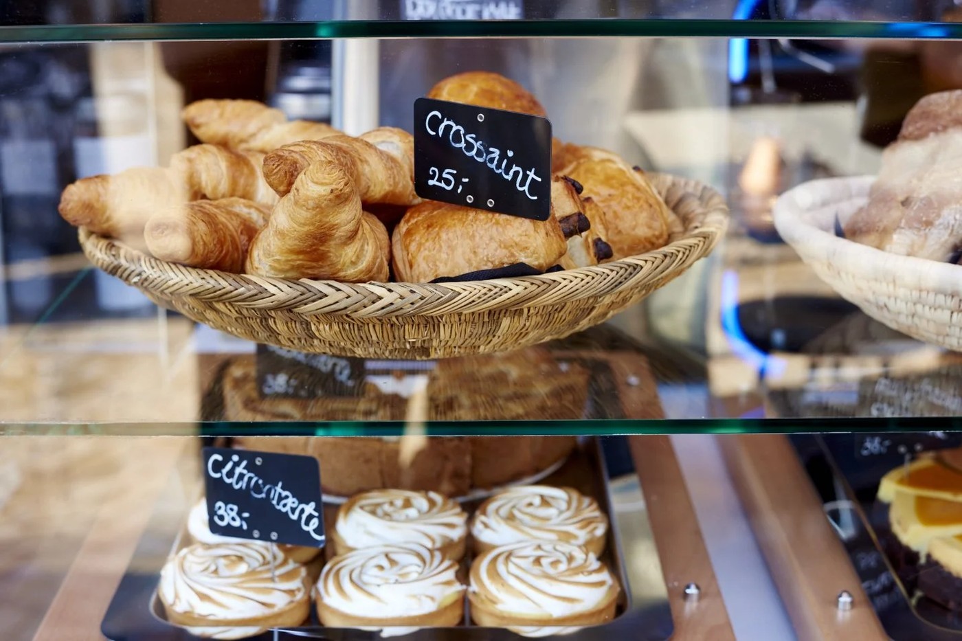 A wicker basket of croissants and pain au chocolat beside a tray of citrontærte in Nelle's pastry case