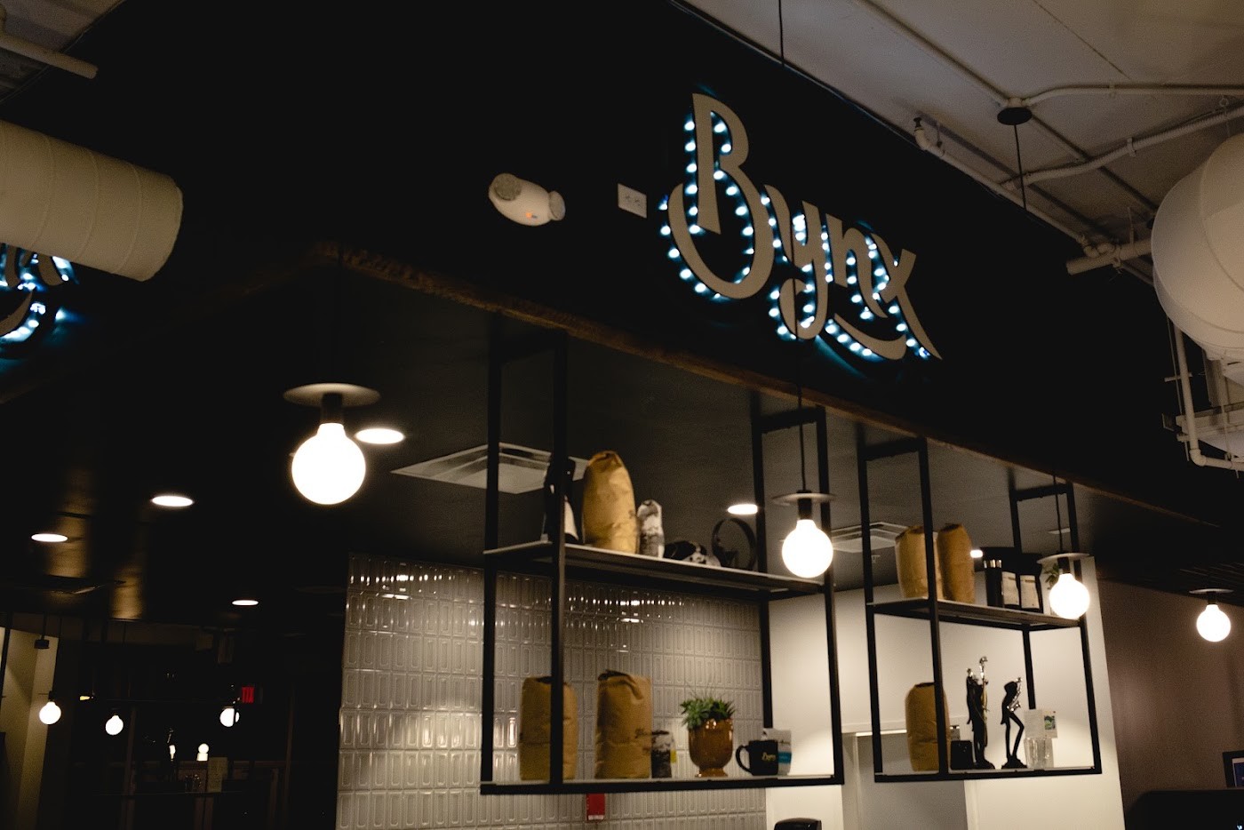 The glowing neon Bynx sign above open shelving holding retail coffee bags and vinyl records