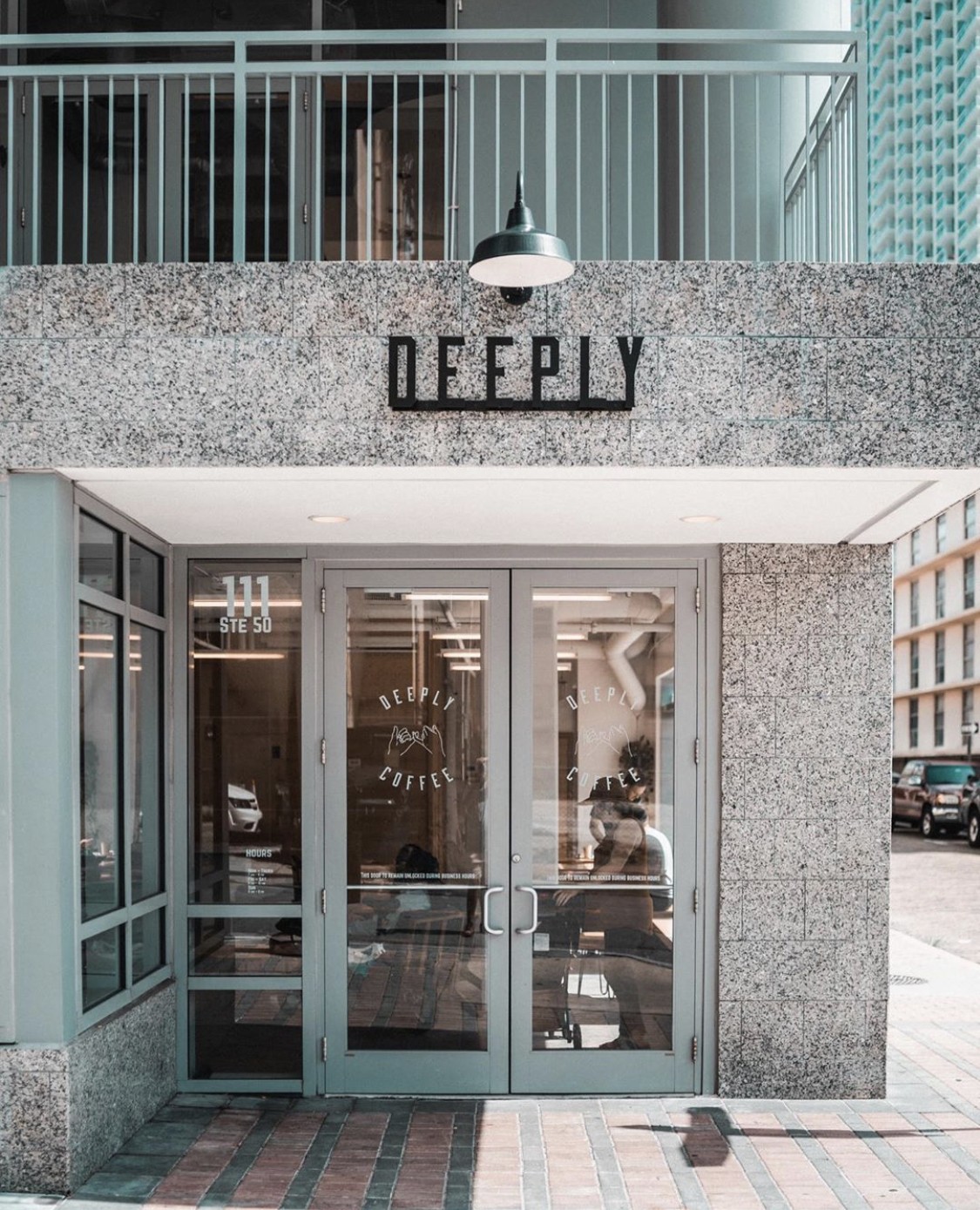 The granite storefront of Deeply with its black wordmark sign above glass double doors etched with the Deeply Coffee logo