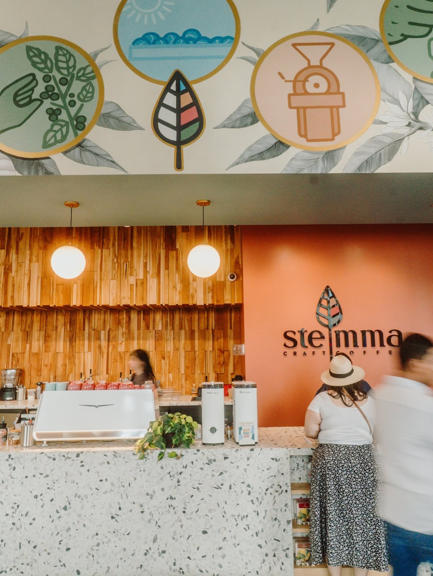 The Stemma Craft Coffee wall logo above a terrazzo counter, with customers ordering beside the espresso bar