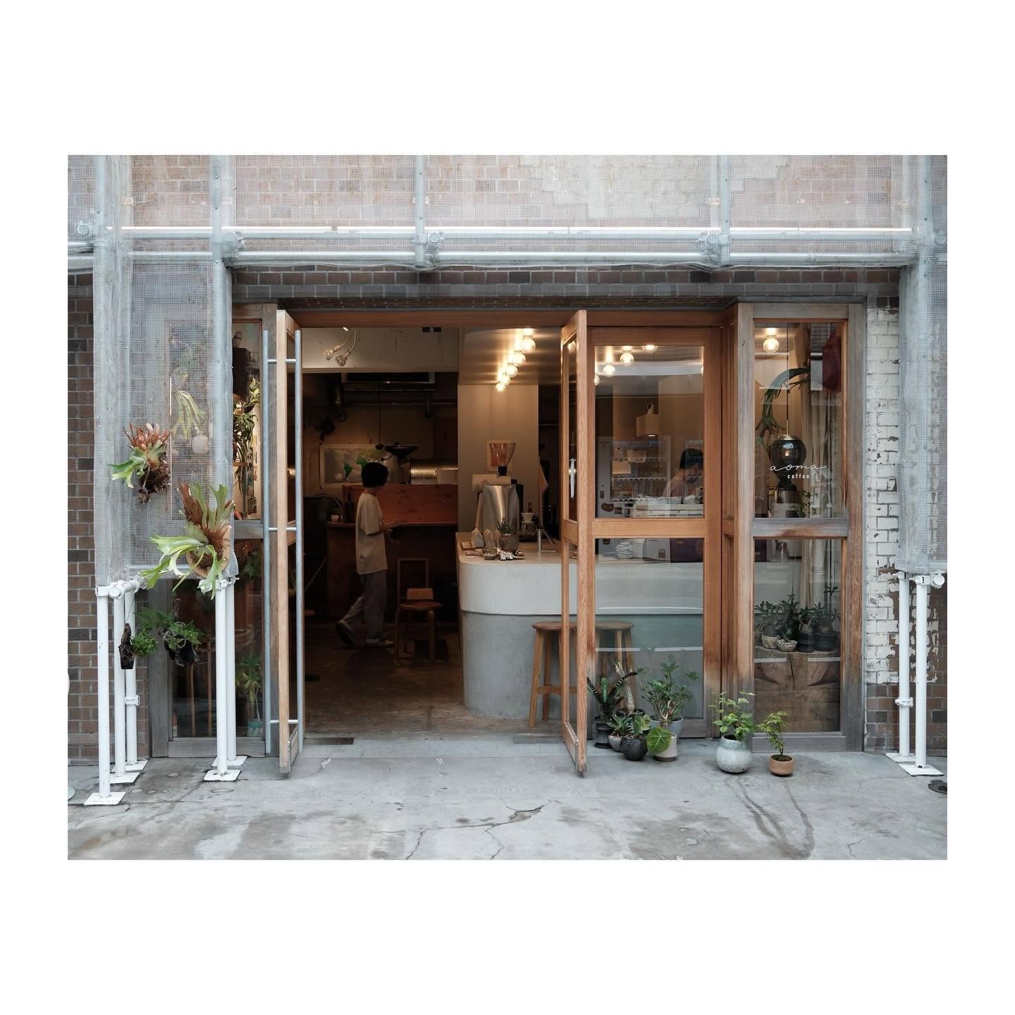 The Aoma Coffee storefront with open wooden doors, hanging plants and a concrete counter visible inside
