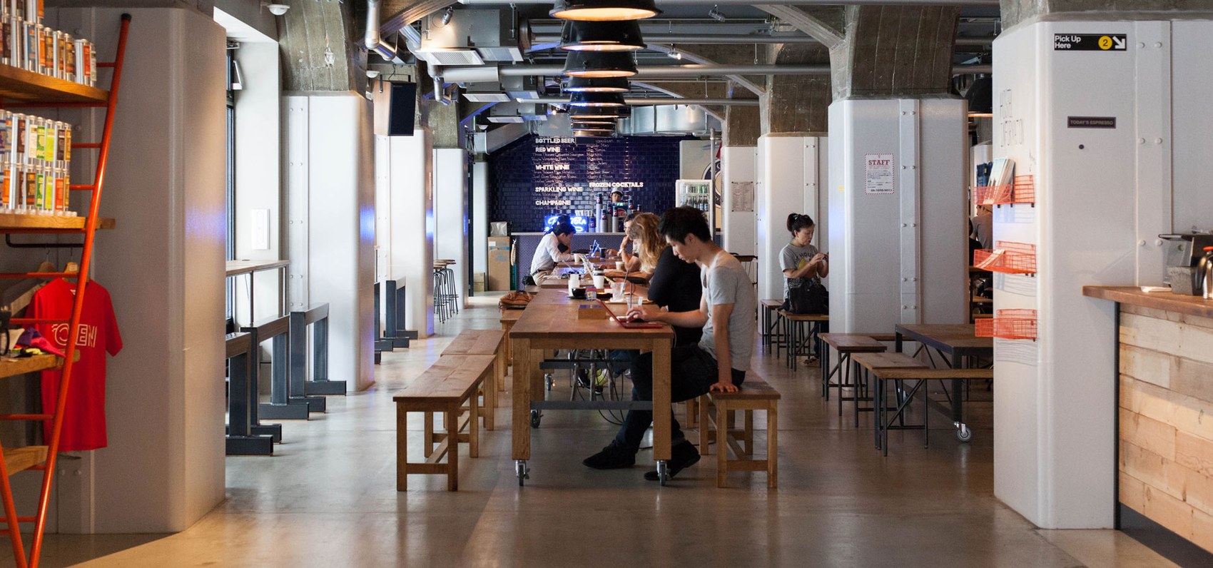 The long communal table room at Brooklyn Roasting Company Namba with customers working on laptops and the drinks menu board behind