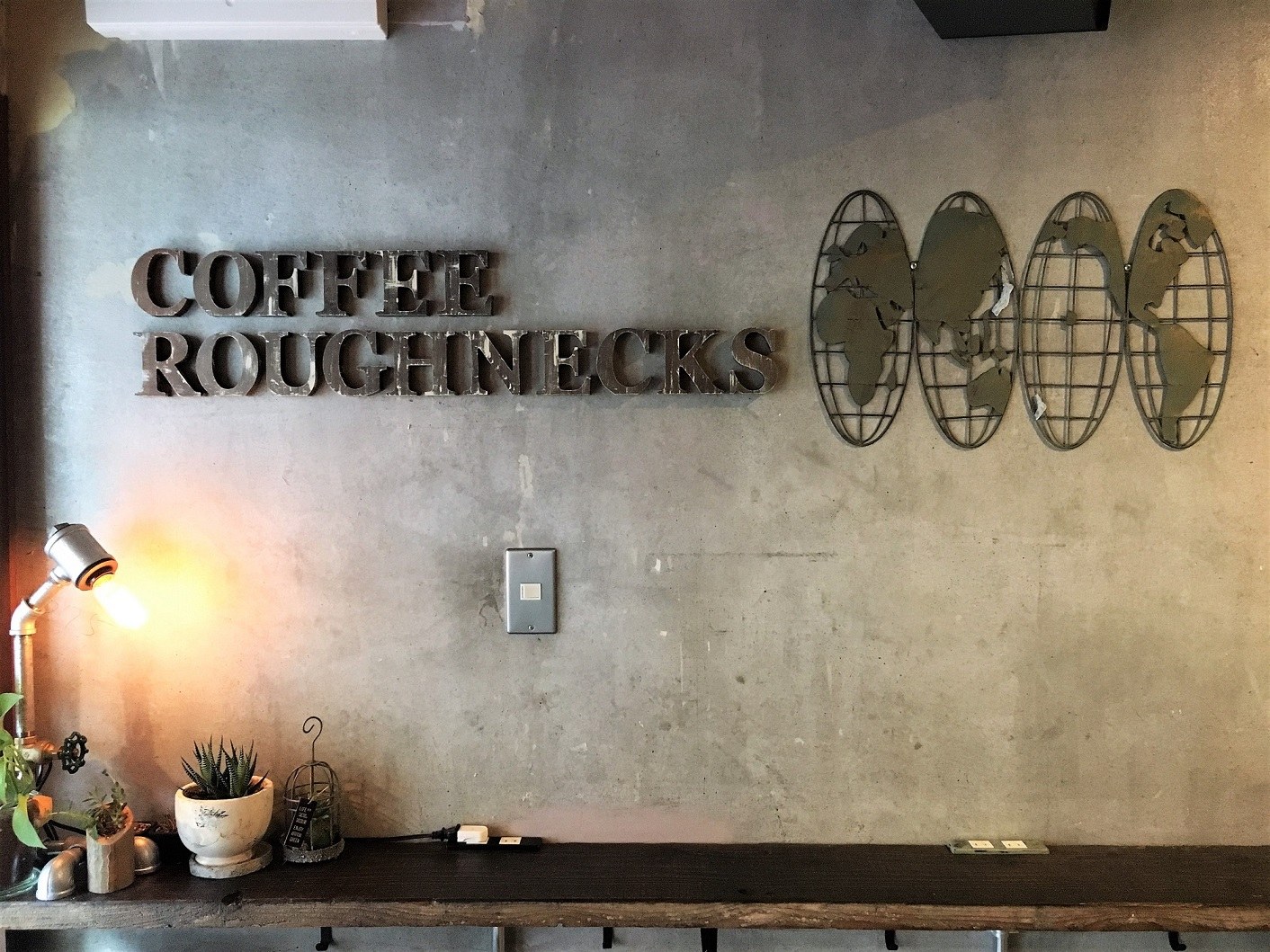 The Coffee Roughnecks wall lettering above a wooden shelf with succulents and a lamp