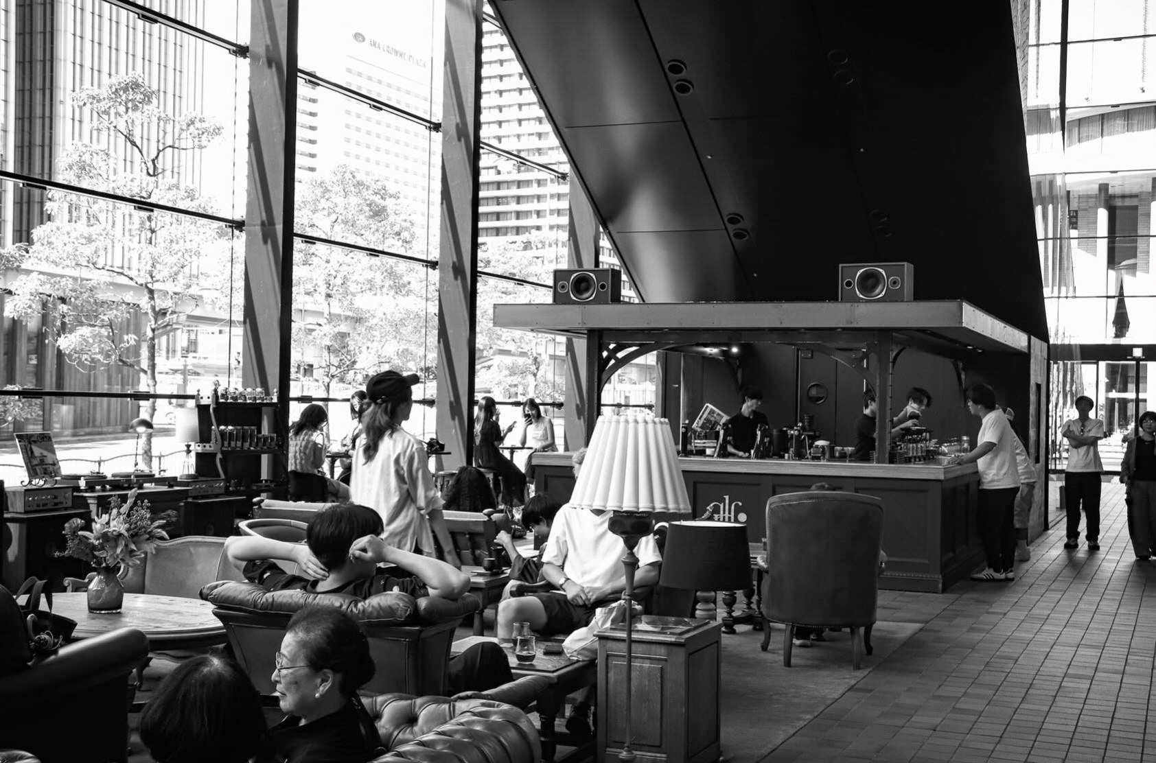 The black curved counter at Glitch Coffee Osaka under floor to ceiling windows, with customers seated in vintage furniture and baristas working the bar