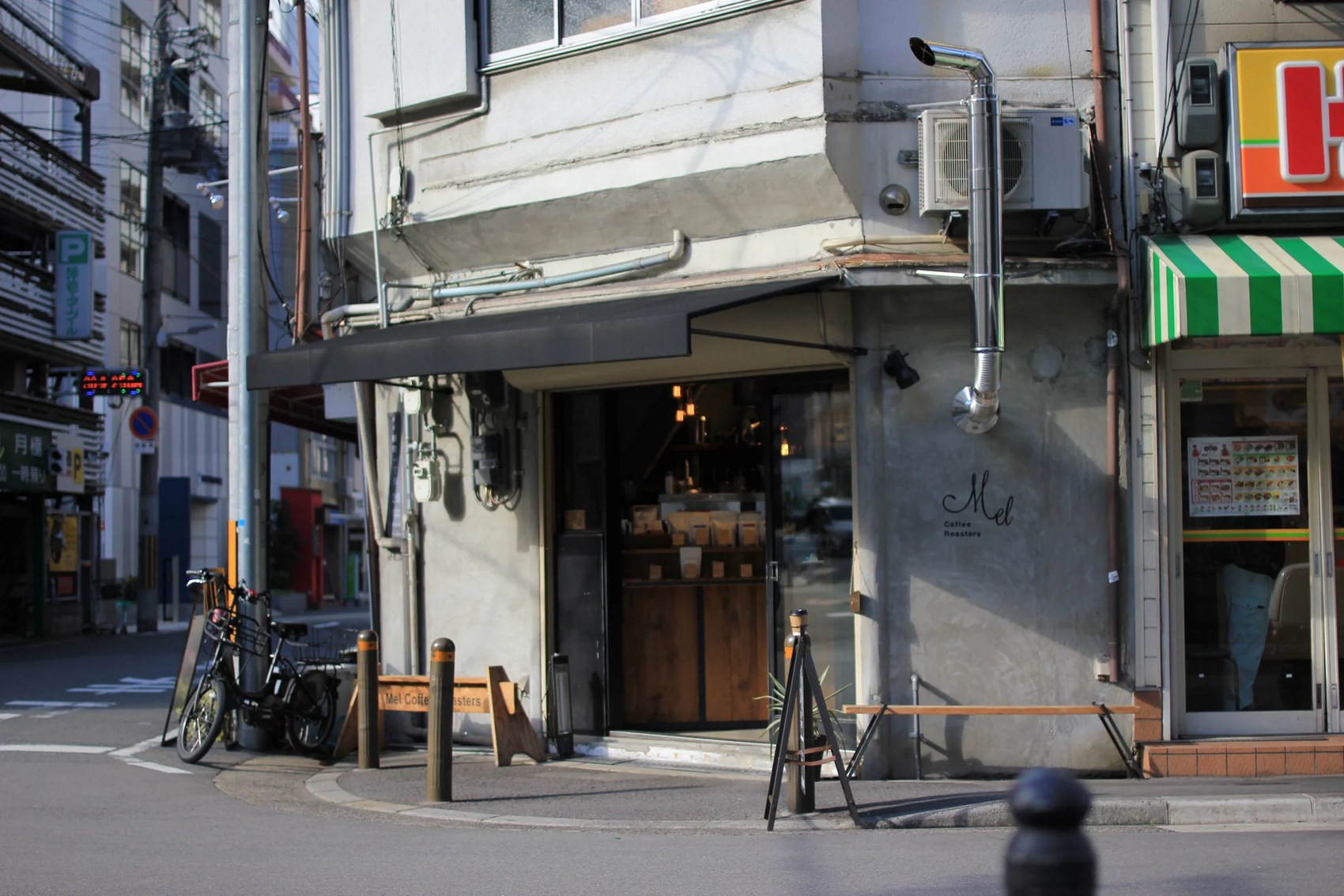 The corner storefront of Mel Coffee Roasters with a black awning and the shop name lettered on the concrete wall
