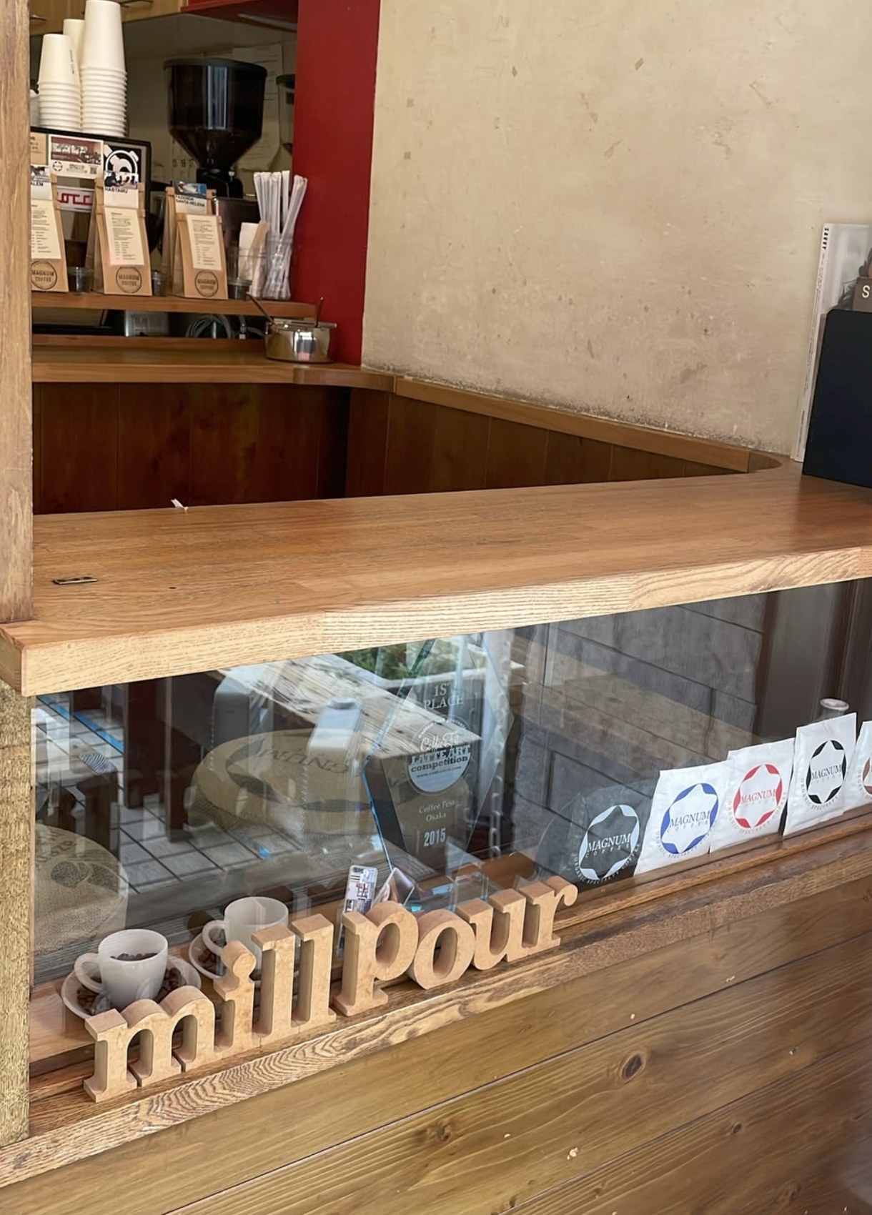 The Mill Pour counter with a wooden millPour sign, retail bean bags and a framed 2015 latte art competition trophy