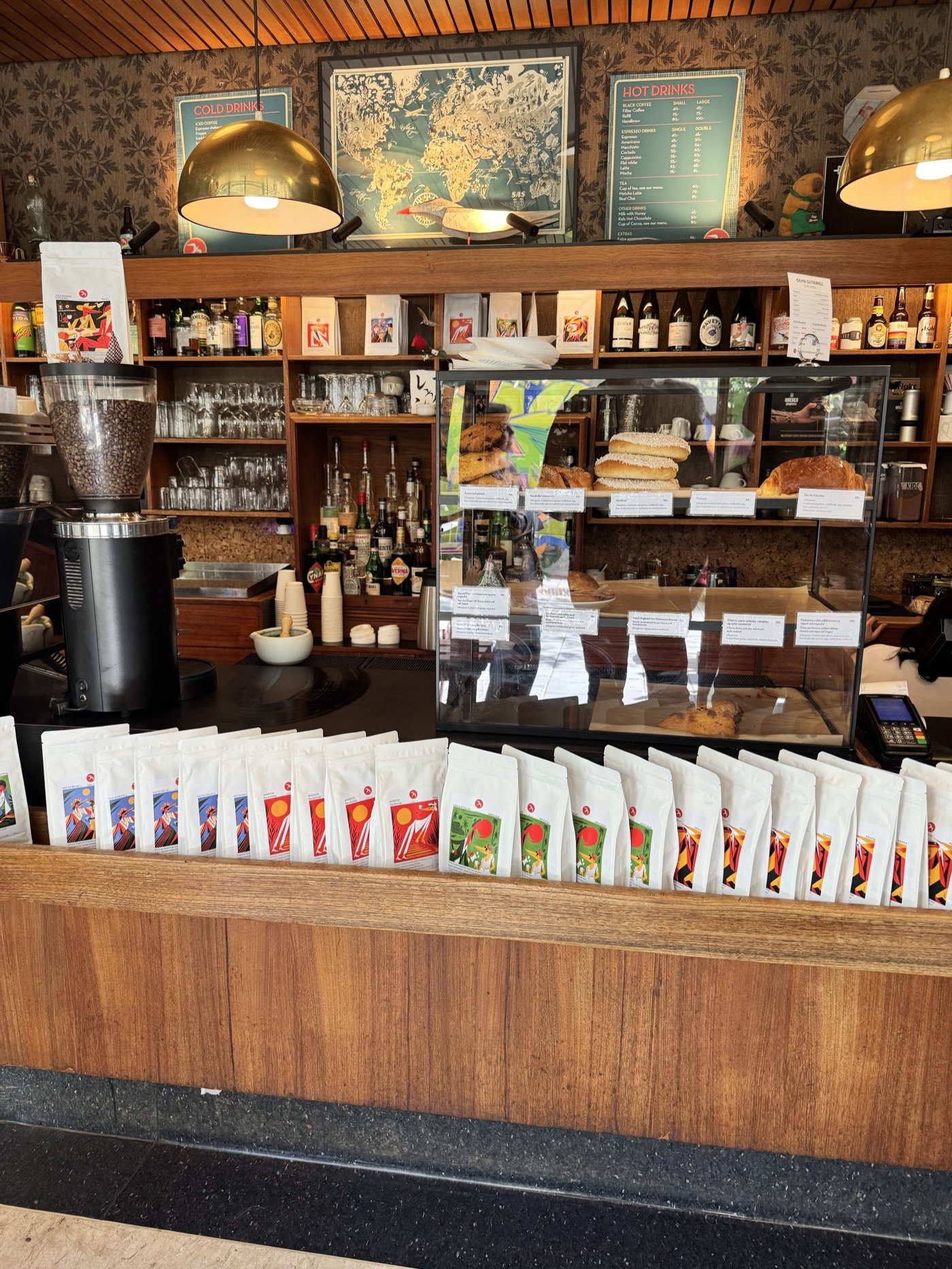 Rows of illustrated Fuglen coffee bags along the counter, with the pastry case, bar shelving, and a world map poster behind