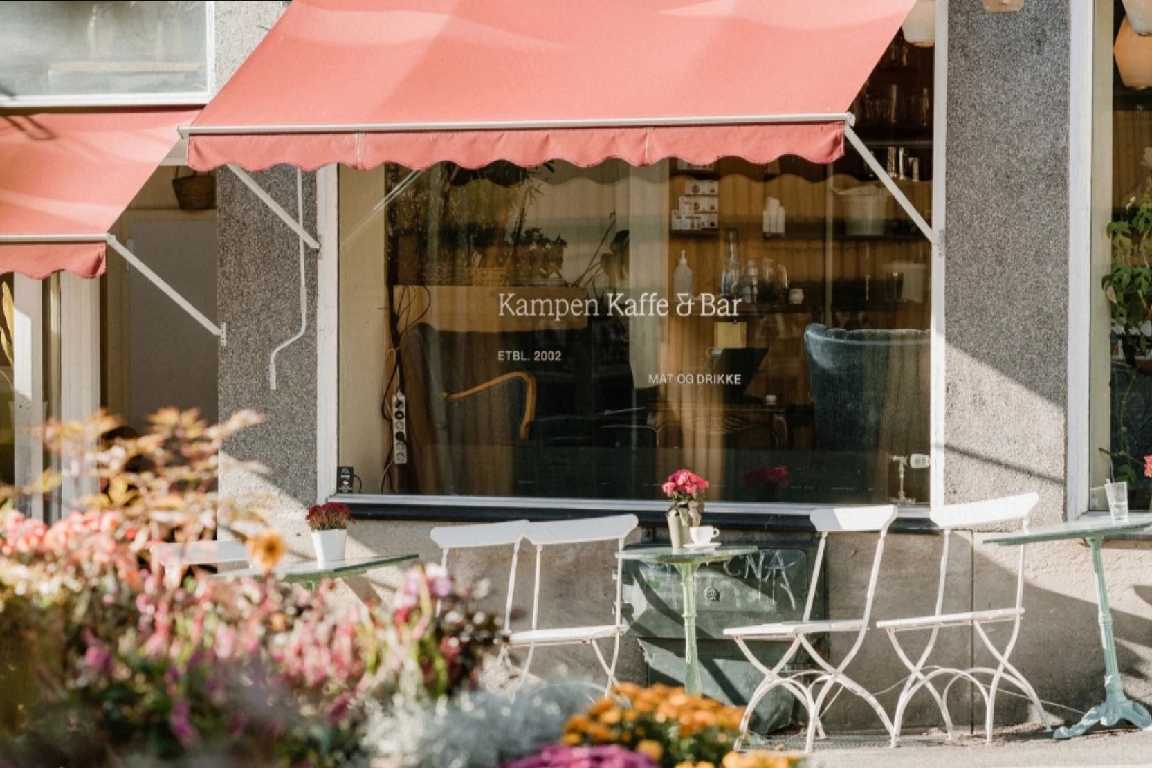 The Kampen Kaffe & Bar storefront, gold window lettering under a coral awning above small outdoor tables and flowers