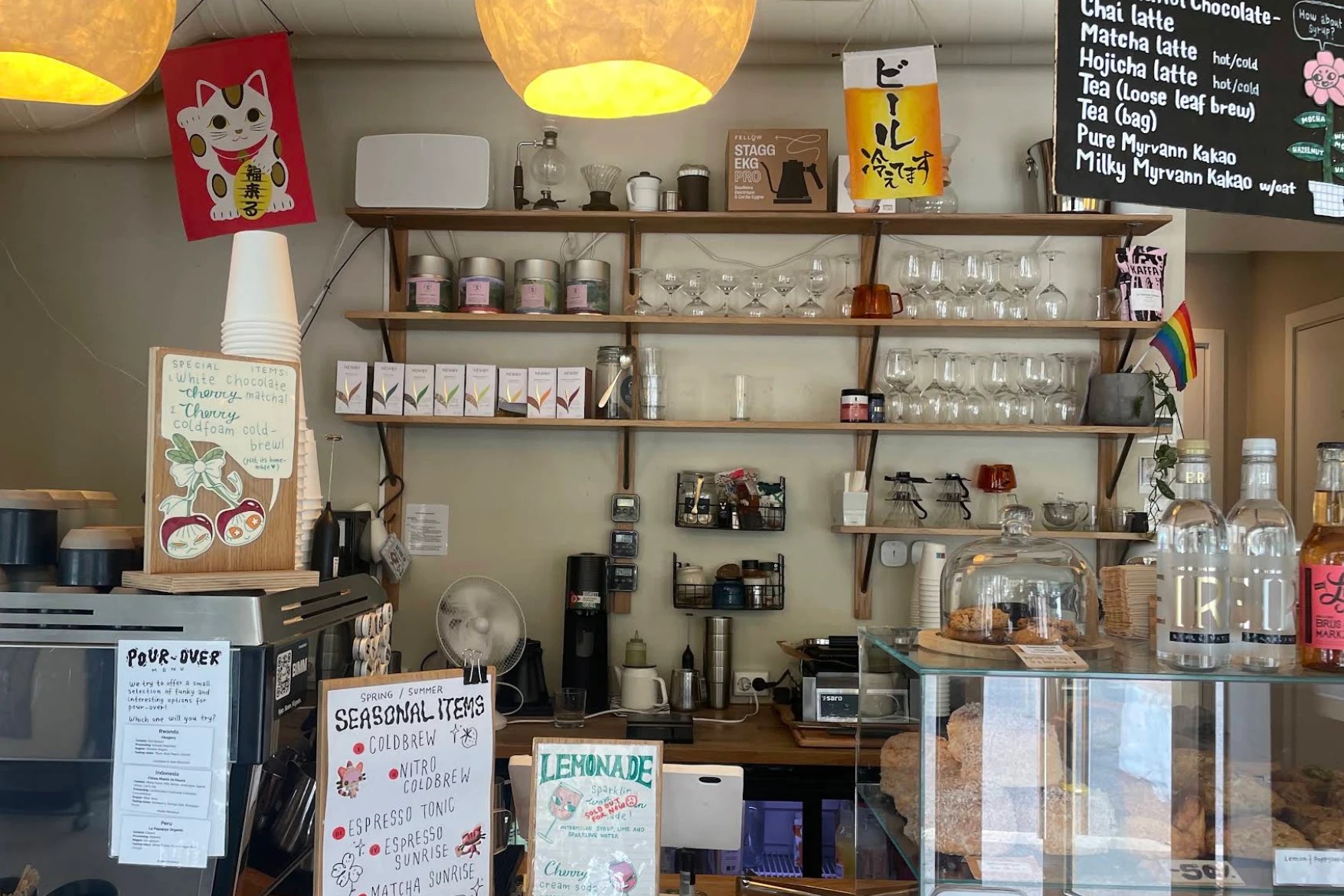 Shelves behind Kuro's counter stacked with tea tins, glassware, and pour-over gear, handwritten seasonal menu boards below