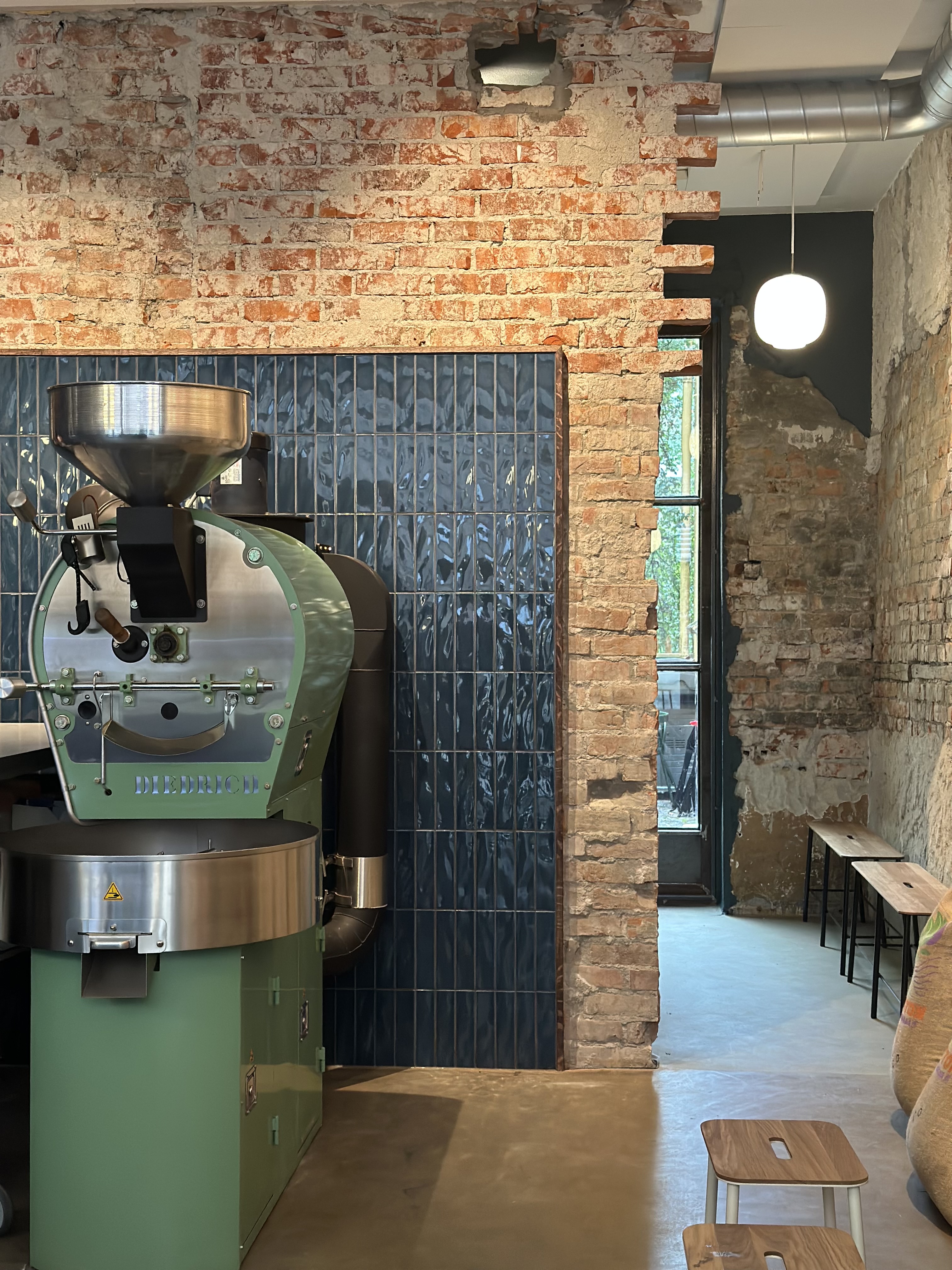 The green Diedrich roasting drum against exposed brick and blue tile inside Lille Oslo Kaffebrenneri