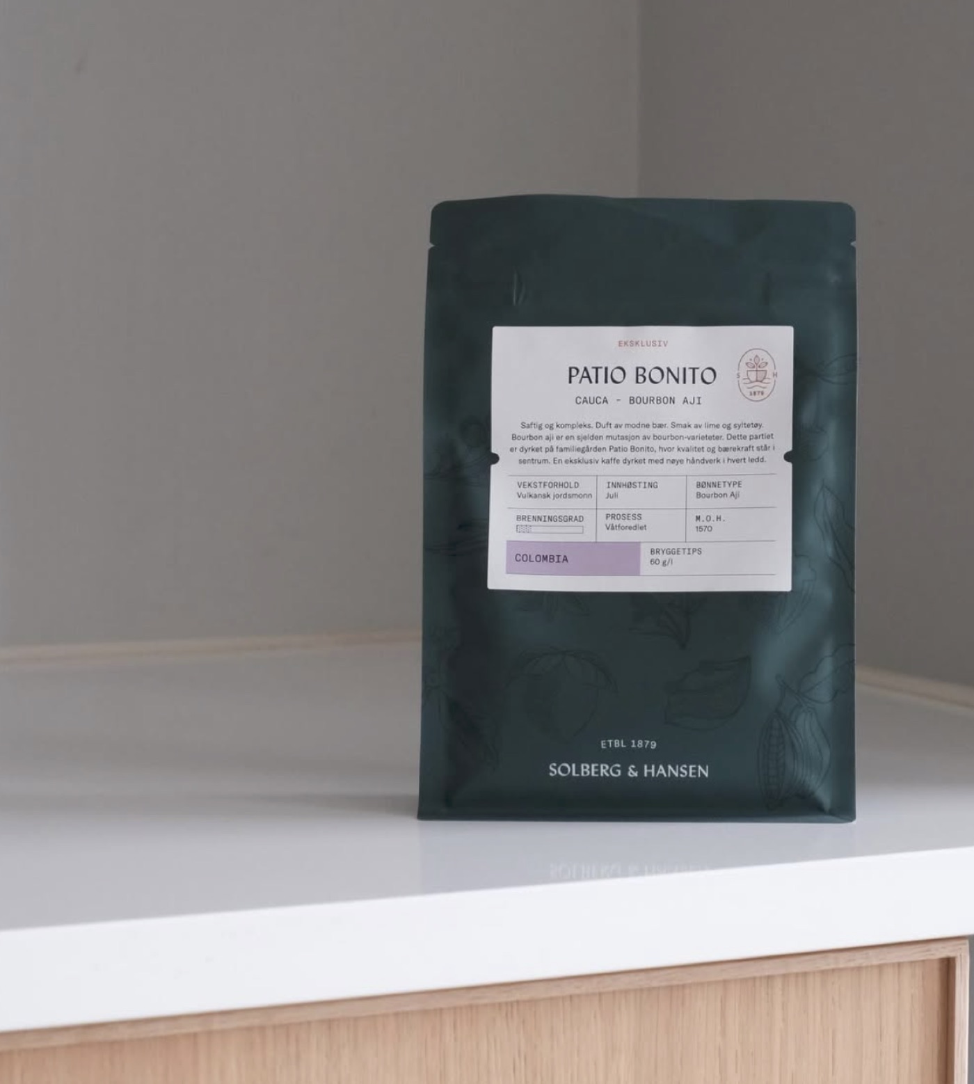 A dark green Solberg & Hansen 'Patio Bonito' coffee bag with its Colombia origin label, standing on a pale wood counter