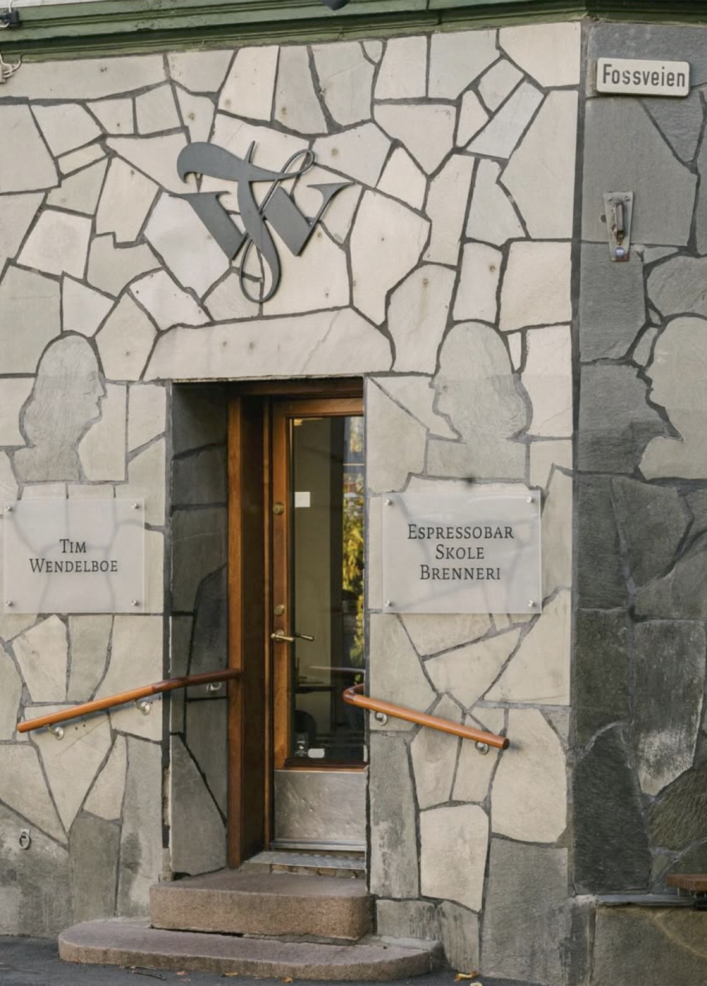The stone entrance of Tim Wendelboe, a metal 'TW' monogram above the door and plaques reading 'Tim Wendelboe' and 'Espressobar Skole Brenneri'