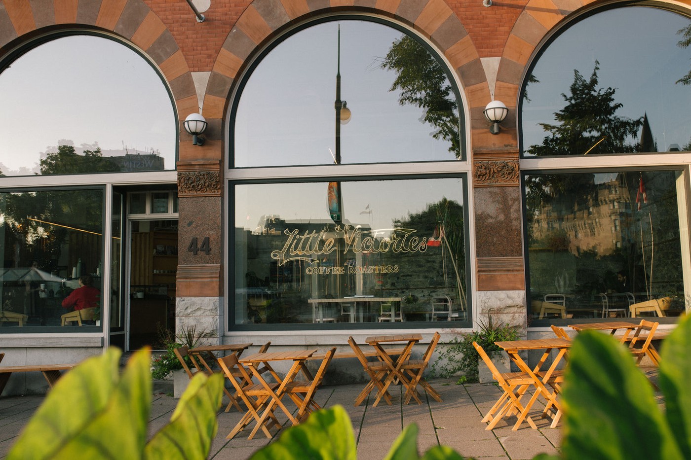 Arched brick storefront of Little Victories Coffee Roasters at 44 Elgin Street, with gold lettering on the window and folding wooden patio tables and chairs outside