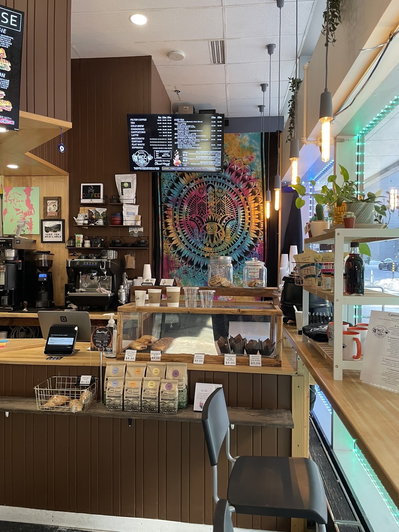 Interior counter of Manhattan's Coffee Co, with a menu board, espresso machine, glass pastry case, and bags of Cloudforest coffee beans on the shelf