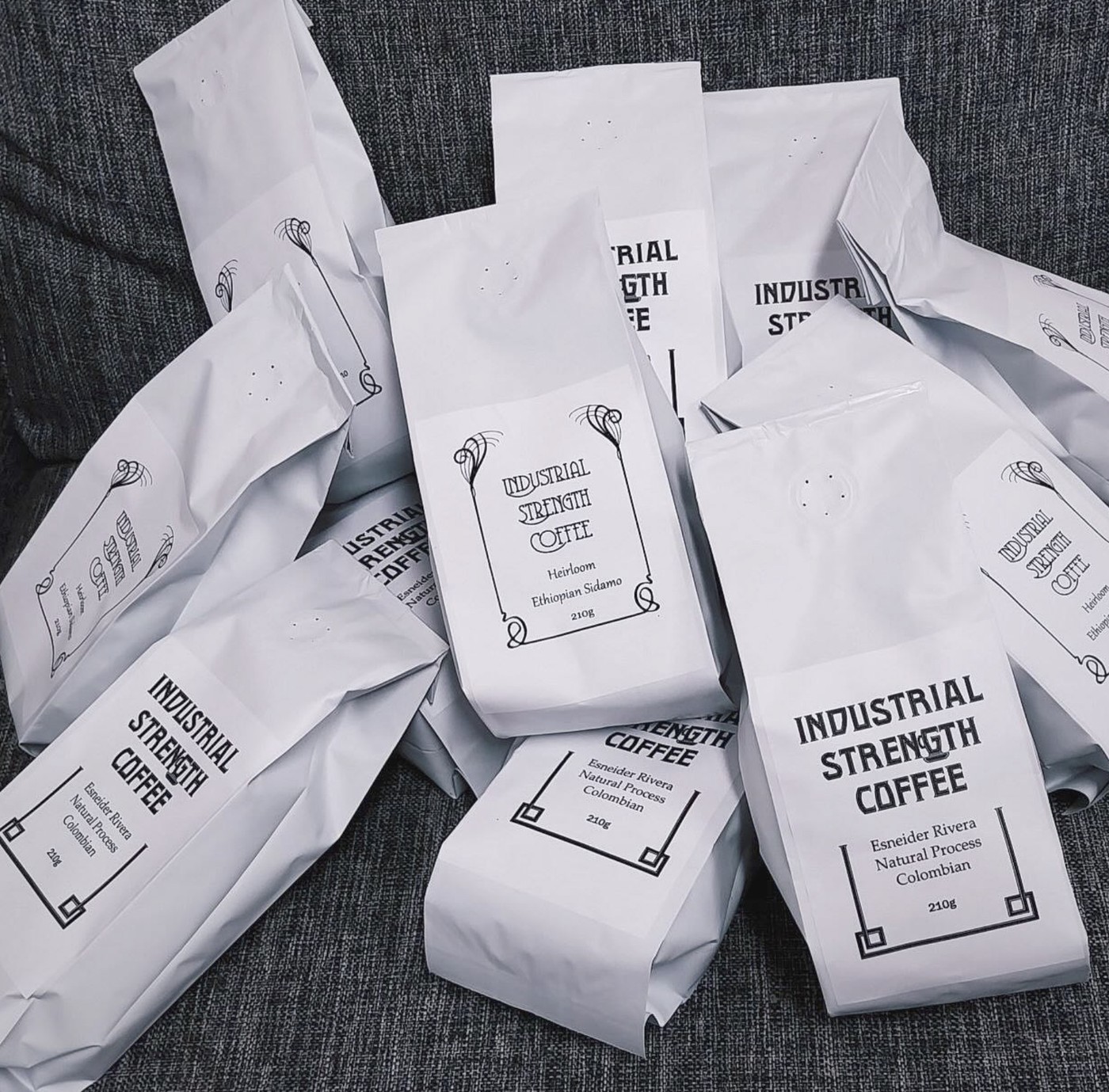 A pile of Industrial Strength Coffee bags in art nouveau style packaging, labeled with single origin Ethiopian Sidamo and Colombian natural process lots